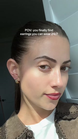 A close-up shot of a young woman's face, looking towards the camera with a slight smile. She is wearing small, decorative hoop earrings. White text is overlaid on the top portion of the image, reading "POV: you finally find earrings you can wear 24/7". The overall aesthetic is casual and relatable, suggesting a personal discovery.