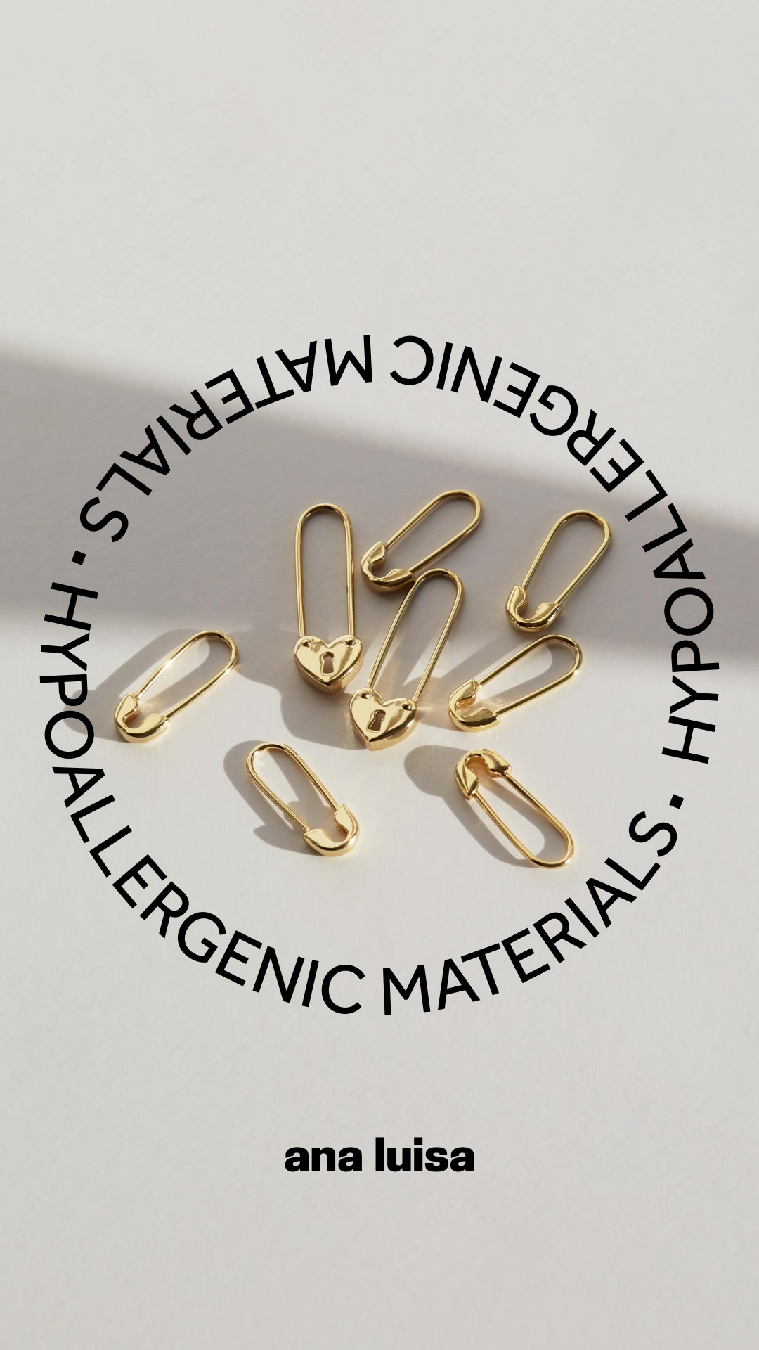 A top-down view of several gold safety pin earrings, some with heart-shaped tops, arranged in a circular pattern on a light grey background. Black text in a circular arc around the earrings reads "HYPOALLERGENIC MATERIALS". Below the earrings, the brand name "ana luisa" is displayed in black text. The ad copy mentions a "Hot Summer Sale" with "20% off EVERYTHING" and states the deal "won't last".