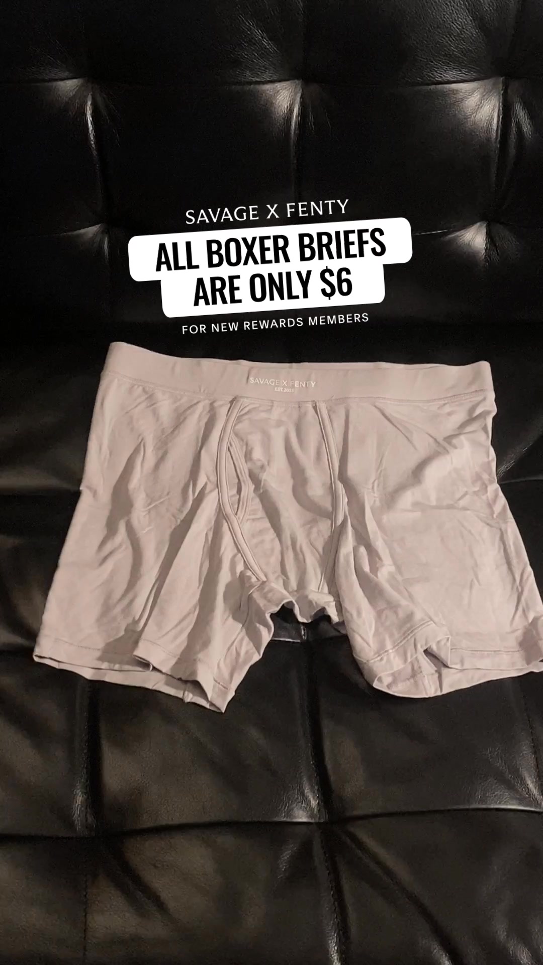 A pair of light grey boxer briefs from Savage X Fenty is laid out on a black, tufted surface. Overlay text in white reads "SAVAGE X FENTY" at the top, followed by a large, bolded white text on a black rounded rectangle that says "ALL BOXER BRIEFS ARE ONLY $6". Below this, in smaller white text, it says "FOR NEW REWARDS MEMBERS".