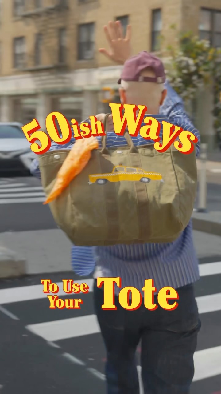 An older man wearing a blue striped shirt and a maroon baseball cap walks across a crosswalk, holding a large olive green tote bag. A carrot sticks out of the bag, and a yellow taxi graphic is printed on the side. Large yellow text with a red outline reads "50ish Ways" across the top of the image. Smaller yellow text with a red outline reads "To Use Your Tote" at the bottom left. The man is waving with his right hand. The background shows a city street with buildings and a car.