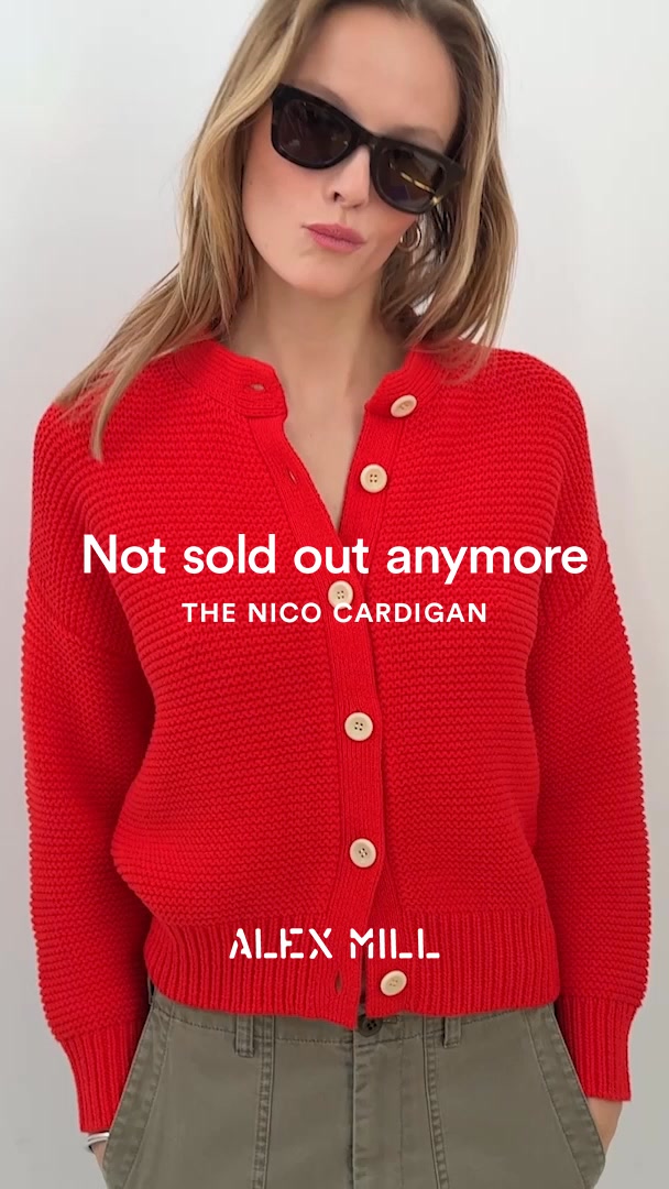 A woman wearing sunglasses and a red knit cardigan stands against a white background. White text overlayed on the image reads "Not sold out anymore" and "THE NICO CARDIGAN". Below that, the brand name "ALEX MILL" is displayed in white text. The woman is looking towards the camera with a slight pout. The cardigan has wooden buttons and the woman is wearing olive green pants.