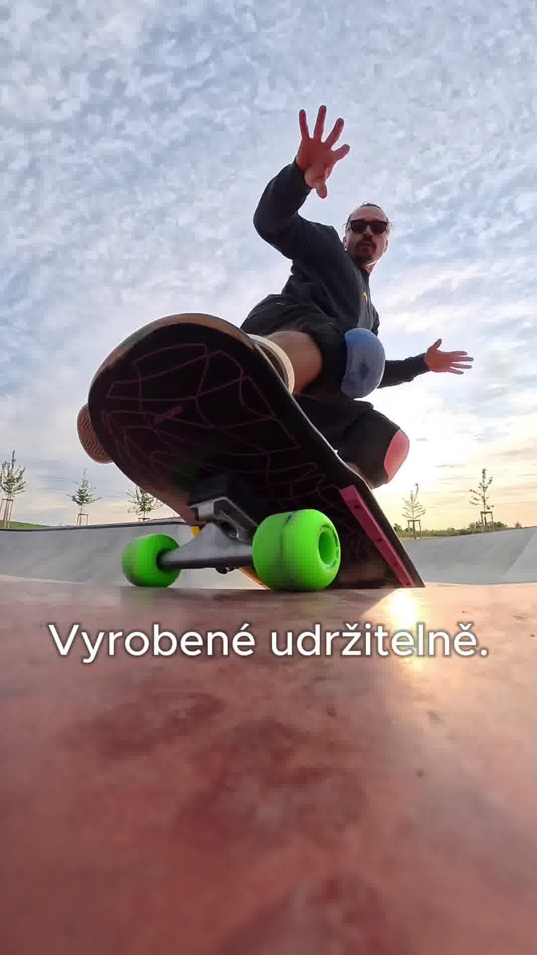 A low-angle shot shows a person in mid-air on a skateboard, wearing protective gear. The skateboard wheels are bright green. The text "Vyrobené udržitelně." is overlaid on the bottom of the image. The background is a cloudy sky and a skatepark. The overall impression is dynamic and action-oriented, with a focus on sustainable production.