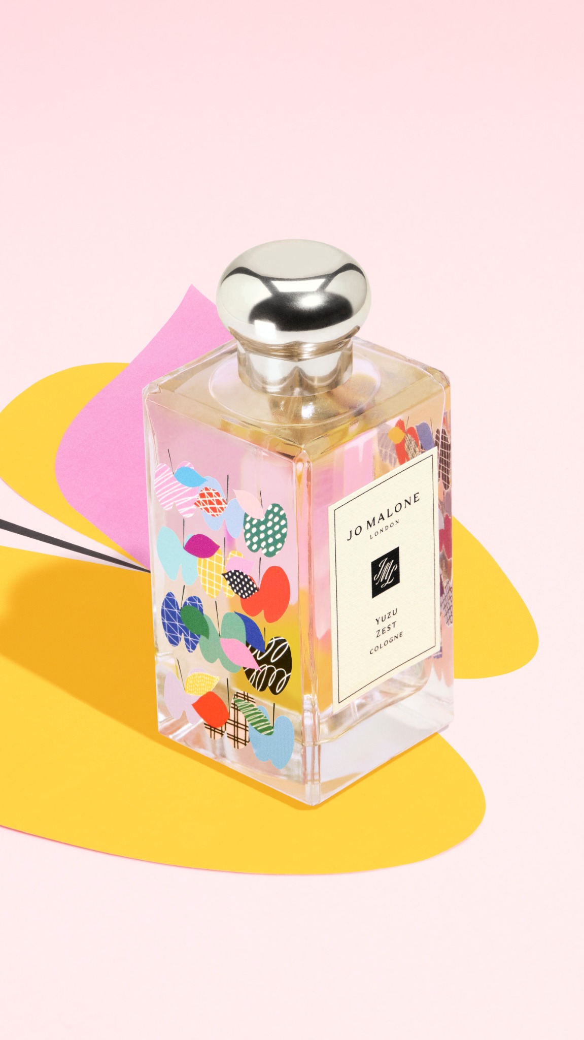 A Jo Malone London Yuzu Zest Cologne bottle is displayed on a pink and yellow abstract background. The bottle has a decorative pattern of colorful shapes and lines. The text overlay introduces the viewer to Jo Malone London's global flagship store in Harajuku, highlighting its size and personalized services like gift customization with exclusive charms and patches. It also mentions Japanese-inspired scents and the store's unique fragrance experience.