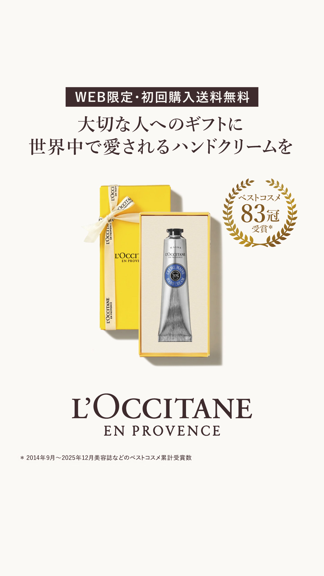 A yellow gift box with a white ribbon is shown next to a box containing a silver tube of hand cream. The text "WEB限定・初回購入送料無料" (WEB Limited, First Purchase Free Shipping) is displayed prominently at the top. Below this, in Japanese, it reads "For a gift to a loved one, a hand cream loved around the world." A circular graphic with "ベストコスメ 83冠 受賞" (Best Cosmetics 83 Crowns Awarded) is on the right side of the image. The L'Occitane en Provence logo is at the bottom.