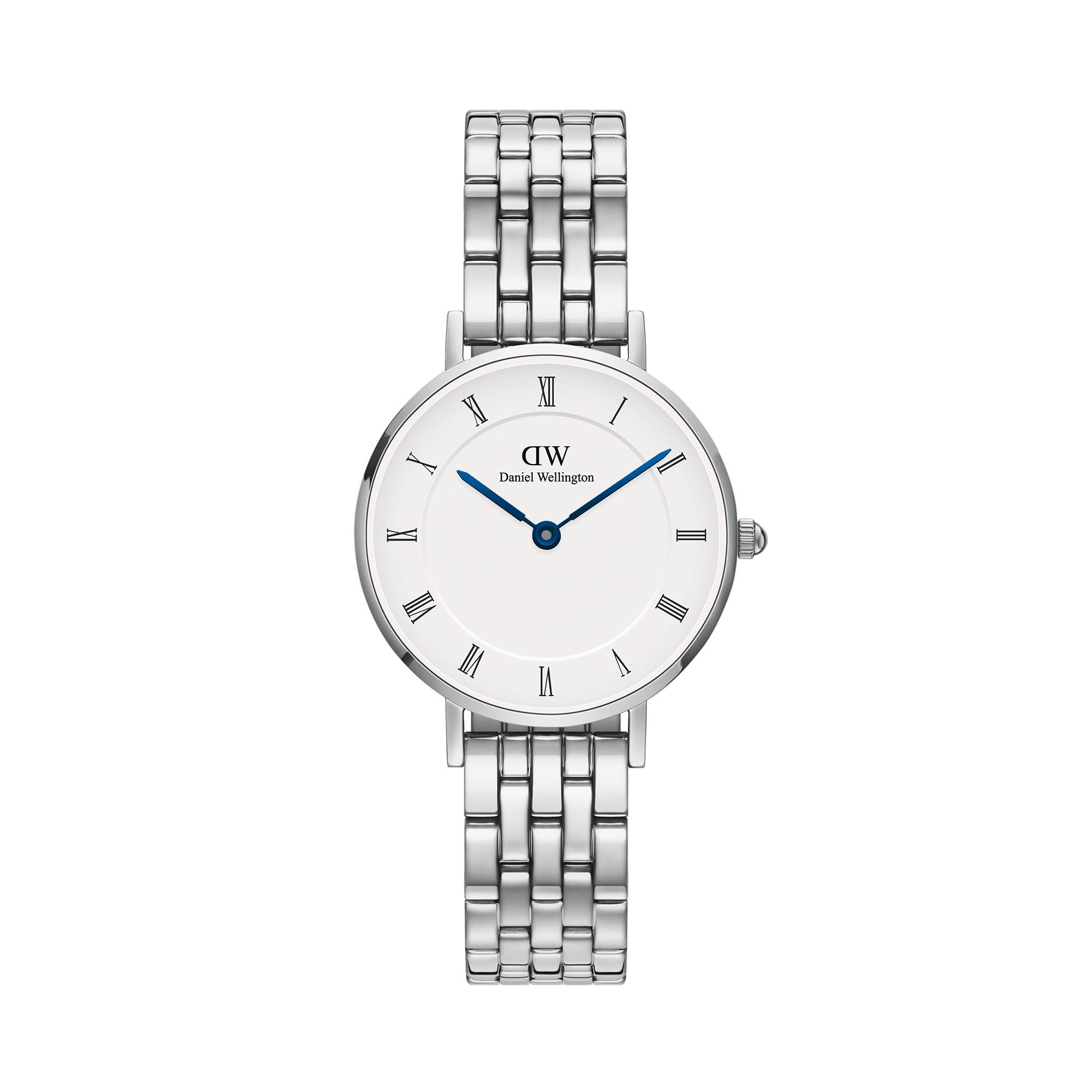 A clean, studio shot of a Daniel Wellington watch with a silver metal band and a white face with Roman numerals. The watch face has blue hour and minute hands. Text overlays read "AW25 is here!" and "Step into a new era of elegance." The creative focuses on the product's aesthetic appeal and suggests a new collection or season.