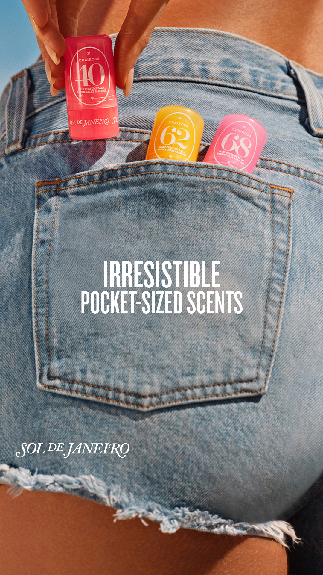 The image shows the back pocket of a pair of denim shorts. Three small, colorful perfume balm containers are tucked into the pocket. A hand is holding one of the containers, pulling it out. White text overlayed on the image reads "IRRESISTIBLE POCKET-SIZED SCENTS" and "SOL DE JANEIRO" at the bottom. The overall aesthetic is summery and casual, highlighting the portability and appeal of the scents.