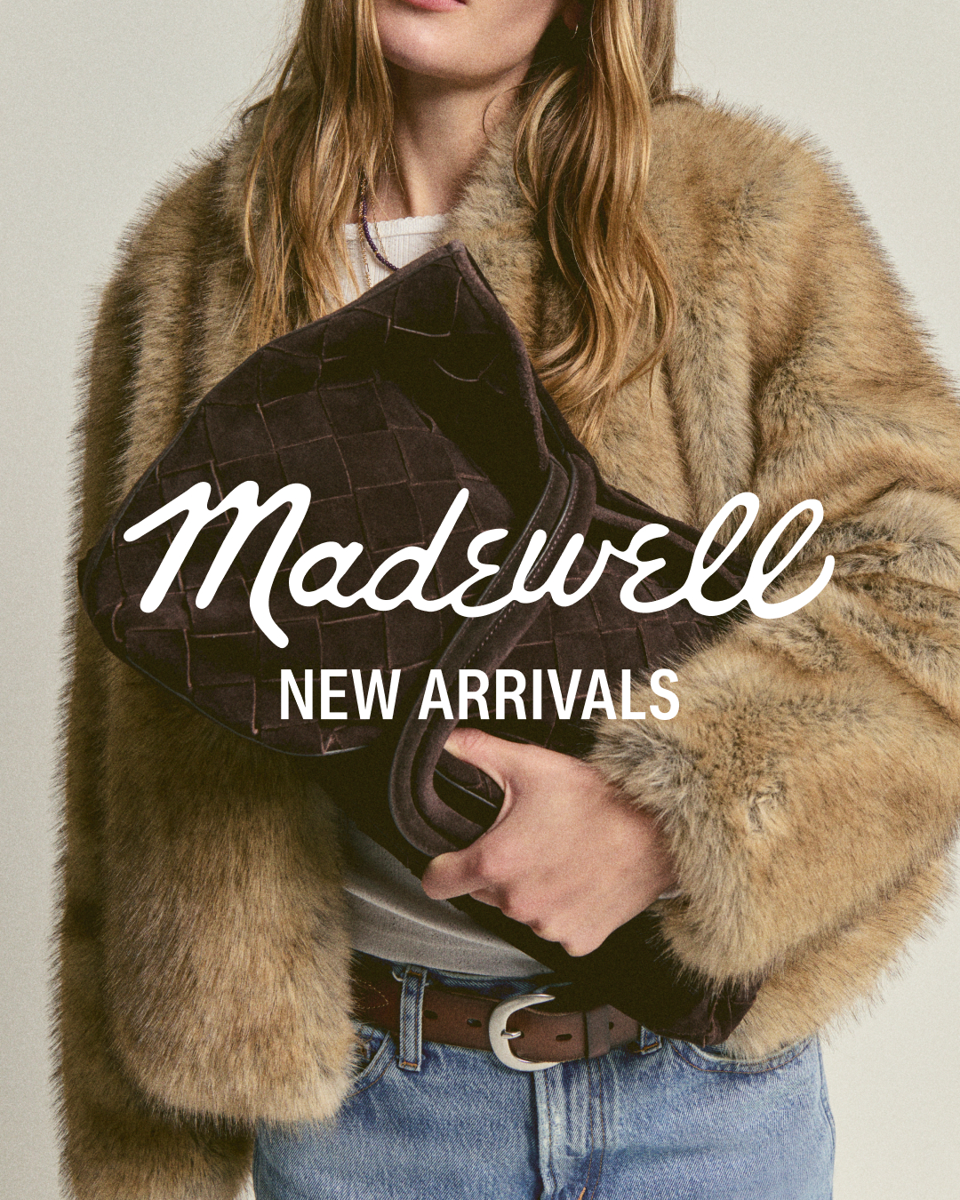 A woman wearing a fluffy tan coat and blue jeans holds a dark brown woven clutch bag. The Madewell logo is overlaid in white script on the upper left of the image, with the text "NEW ARRIVALS" below it in a sans-serif font. The overall aesthetic is chic and fashionable, suggesting timeless style and quality pieces that can be worn for multiple seasons.