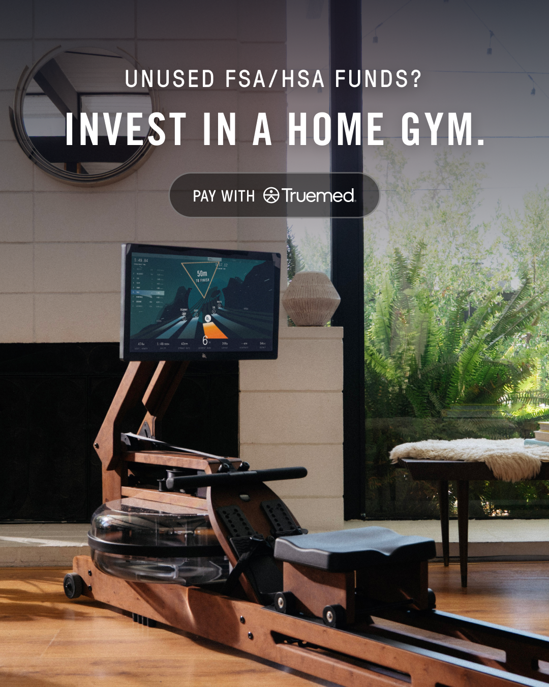 A high-end wooden rowing machine is shown in a well-lit, modern living room with a large window overlooking lush greenery. The screen of the rowing machine displays workout metrics. Overlay text asks, "UNUSED FSA/HSA FUNDS? INVEST IN A HOME GYM." Below this, it states, "PAY WITH Truemed."