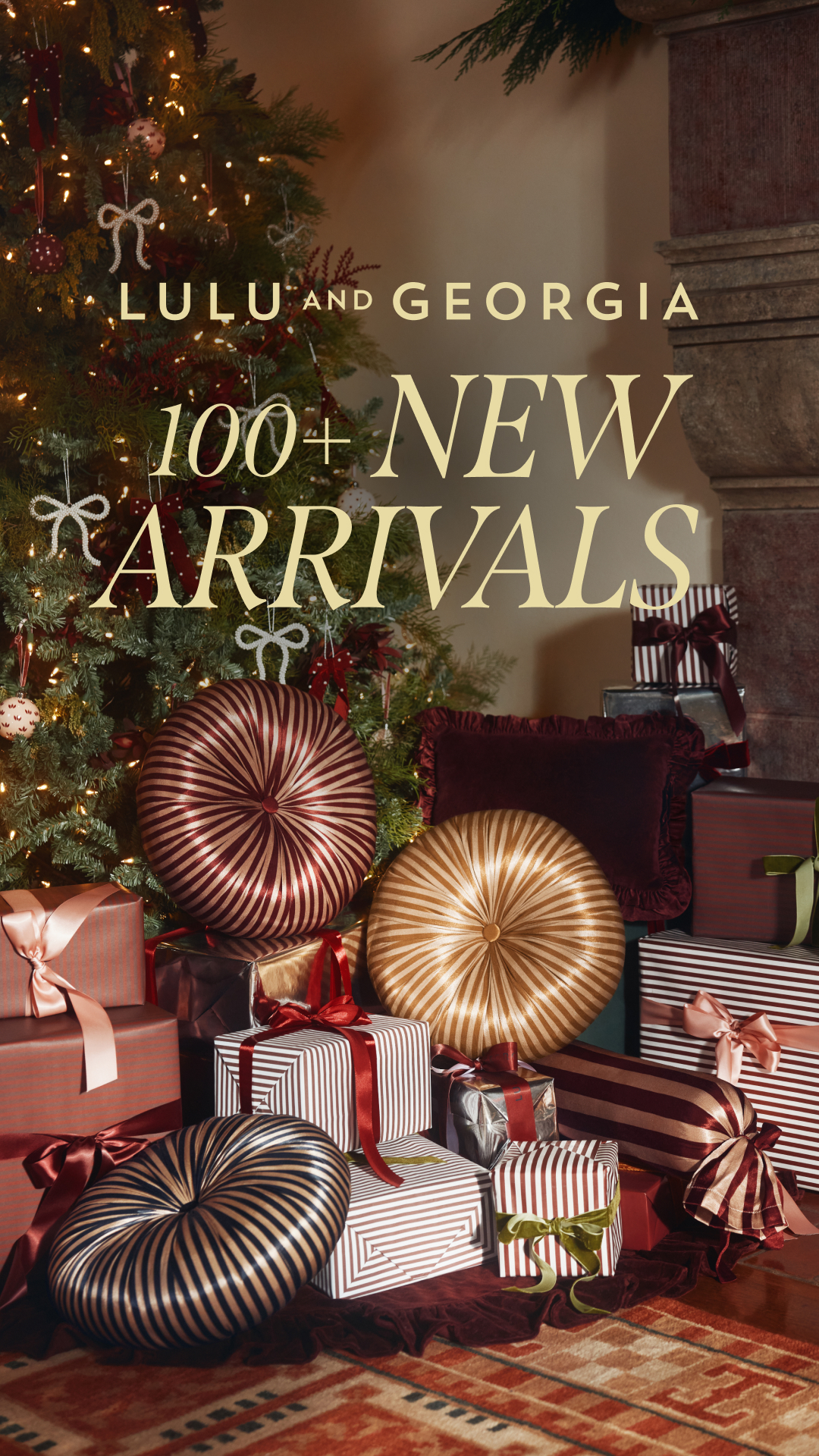 A festive scene is depicted with a decorated Christmas tree on the left and a stone fireplace on the right. Piles of elegantly wrapped gifts are arranged in front of the tree and fireplace. The text "LULU AND GEORGIA" is displayed prominently at the top, followed by "100+ NEW ARRIVALS" in larger font below it. The overall image evokes a sense of holiday abundance and new product offerings.