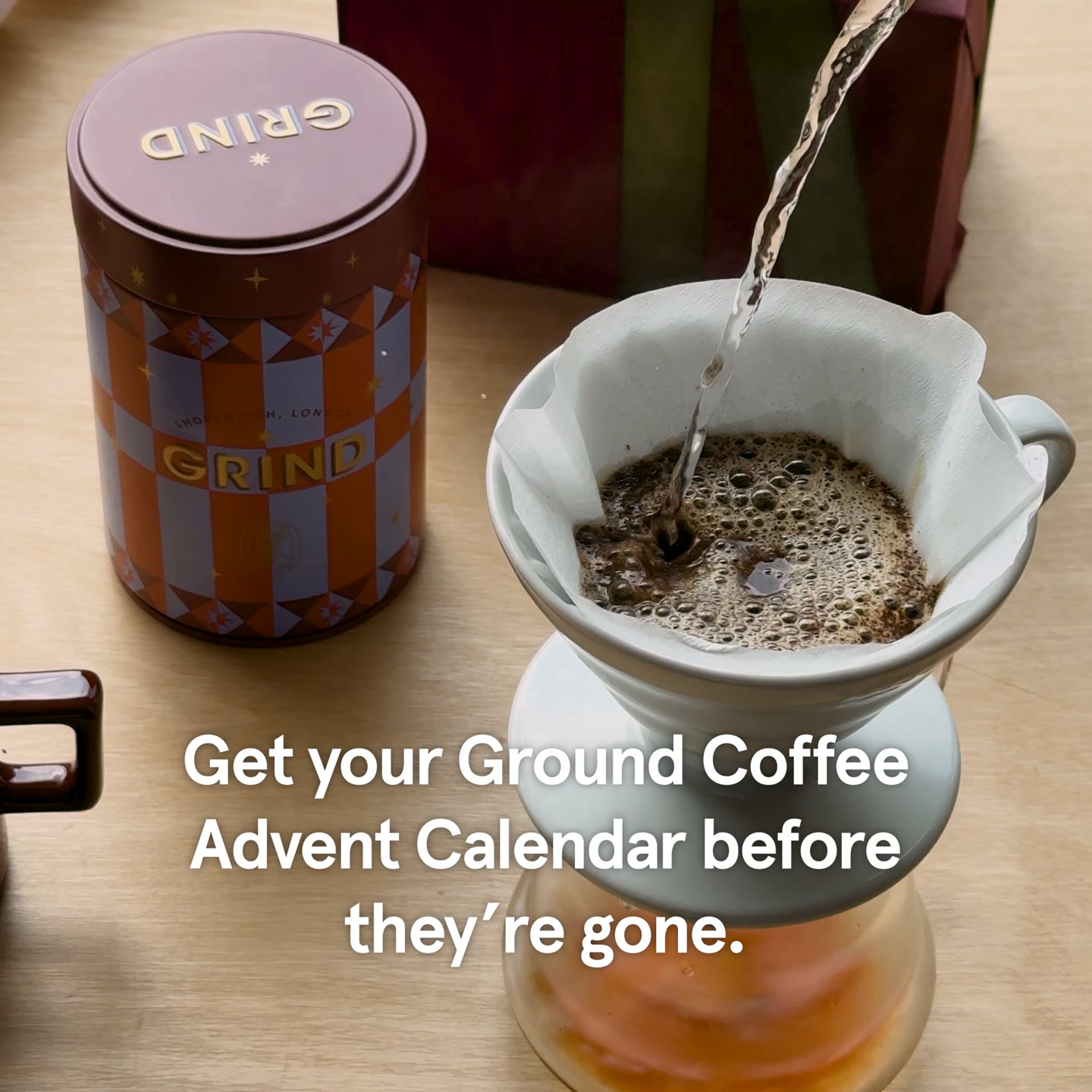 A close-up shot shows coffee grounds being brewed in a pour-over coffee maker. To the left, a decorative tin labeled "GRIND" is visible, with a festive gift box in the background. White text overlaid on the image reads: "Get your Ground Coffee Advent Calendar before they're gone."