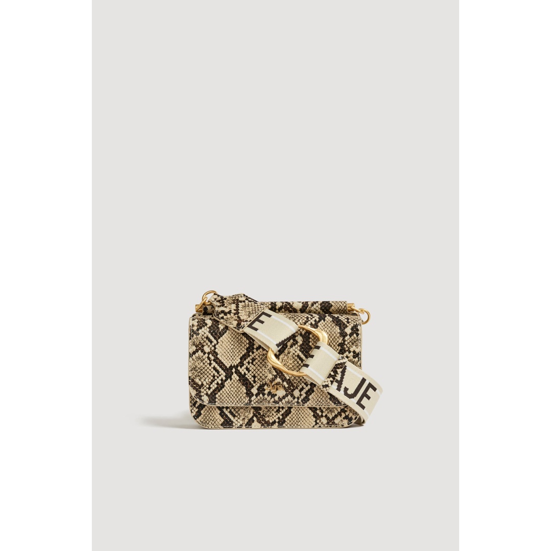 A close-up studio shot of a small, rectangular handbag with a snakeskin print. The bag has a flap closure and a thick, cream-colored strap with black lettering that reads "E AJE". The strap is adorned with a gold buckle. The background is a plain, light gray, isolating the product. The on-screen text reads: "For women who dress with intention. This is Aje."