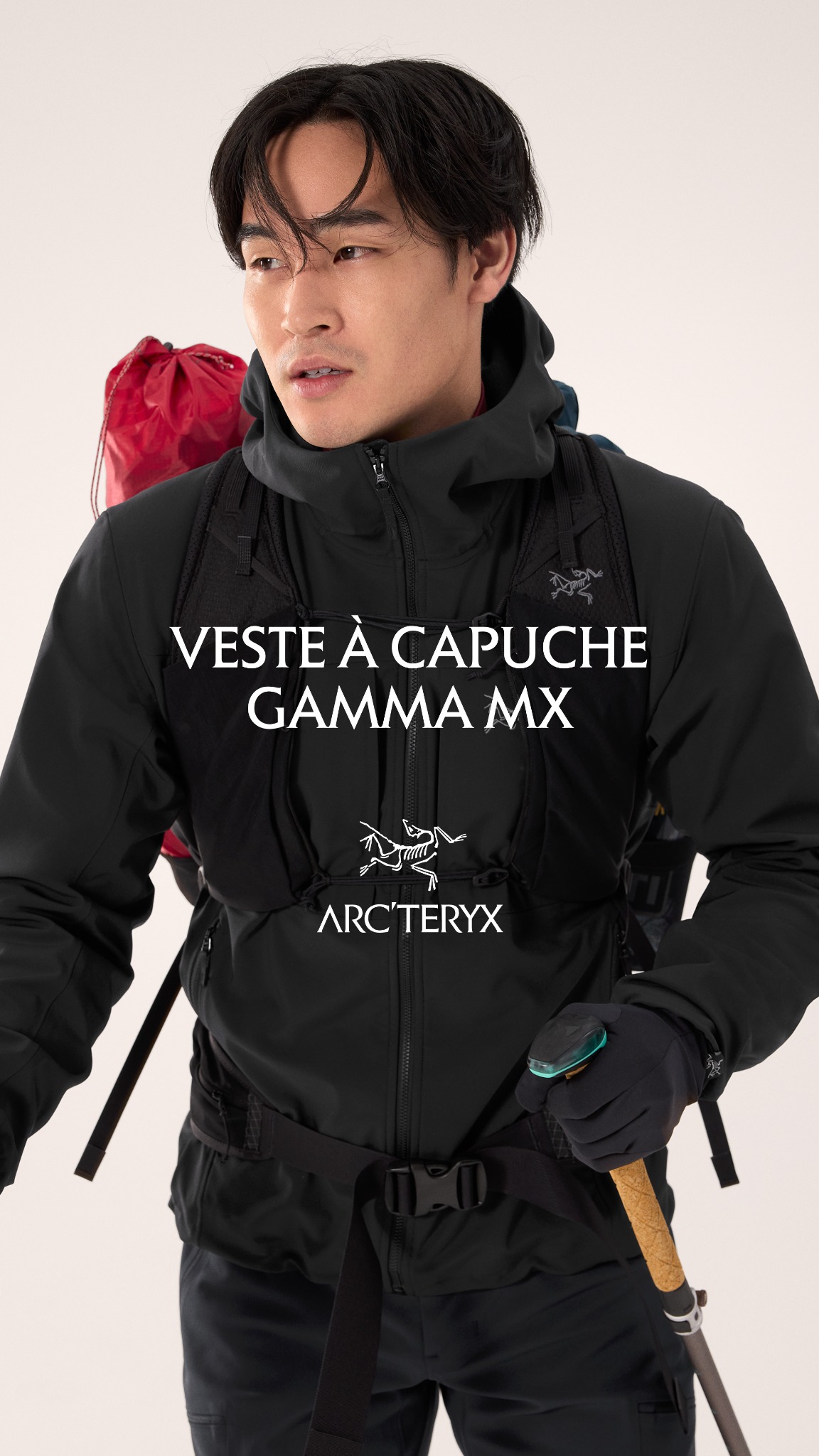 A man wearing a black Arc'teryx jacket and dark pants is shown from the chest up. He is wearing a backpack with a red bag on top and holding a hiking pole. White text overlaid on the image reads "Veste à capuche Gamma MX" and the Arc'teryx logo is visible. The copy describes the jacket as weather-resistant, durable, insulating, and easy to layer with a new looser fit.