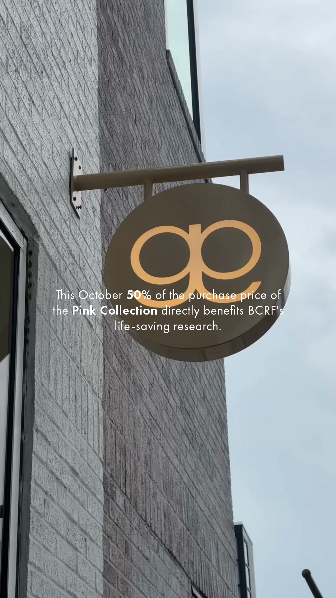 A close-up shot of a building facade with a hanging sign that has the Gorjana logo. White text is overlaid on the bottom half of the image. The text reads: "This October 50% of the purchase price of the Pink Collection directly benefits BCRF's life-saving research." The hook is "gorjana gives back." The ad is promoting a limited-time offer for October, where a portion of proceeds from the Pink Collection goes to BCRF.