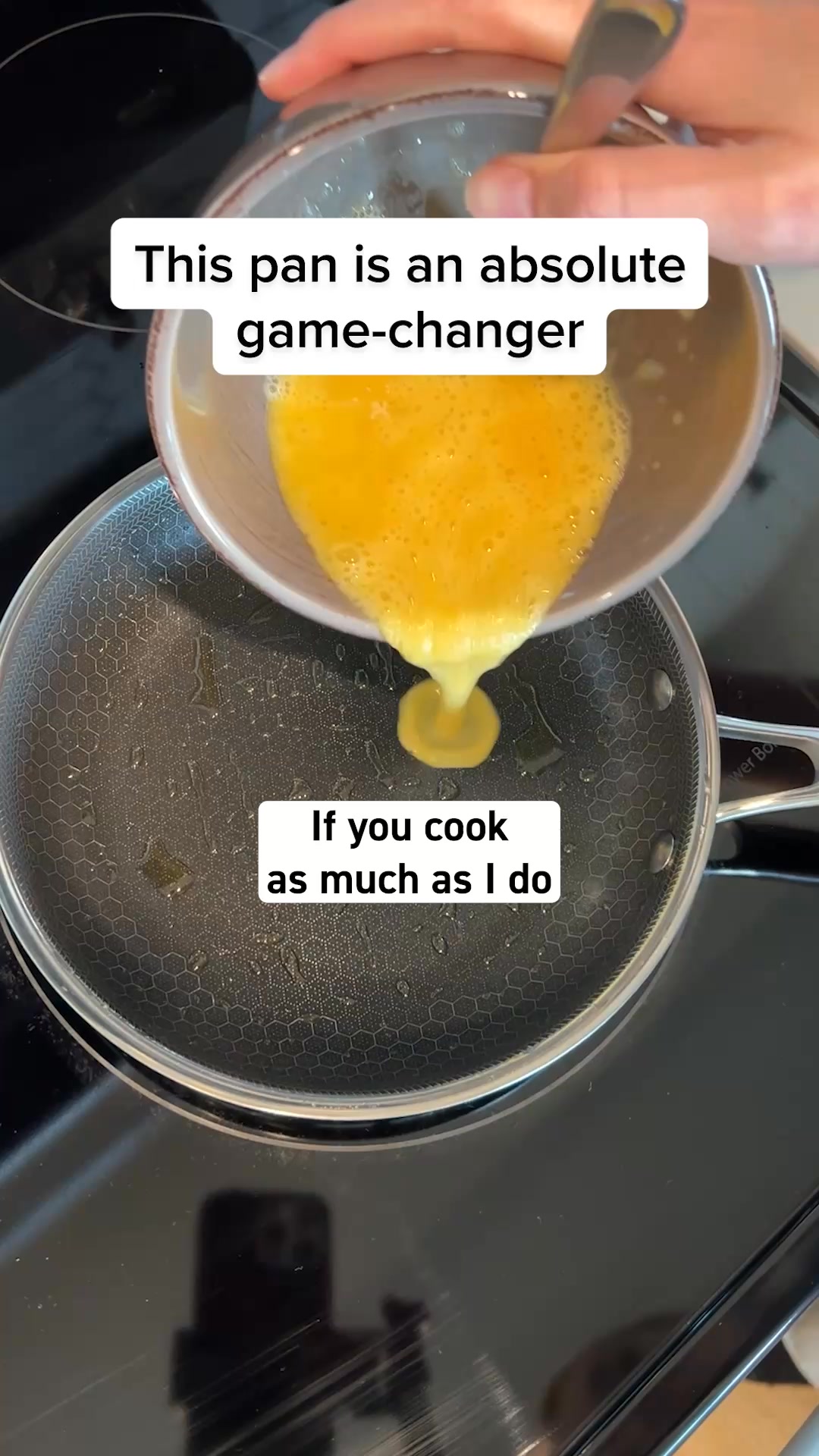 The creative shows a close-up of a non-stick frying pan on a stovetop. Beaten eggs are being poured from a bowl into the pan. White text overlays on the image read "This pan is an absolute game-changer" and "If you cook as much as I do". The focus is on the pan's surface and the cooking process.