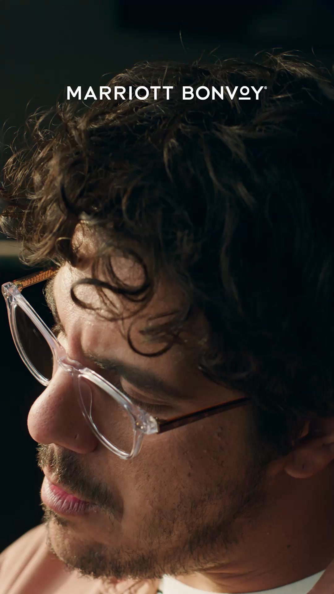 The creative features a close-up, profile view of a man wearing clear-rimmed glasses. The Marriott Bonvoy logo is prominently displayed in white text at the top of the image. The text overlay on the image reads, "Discover views that bring out your inner artist, explore our entire world of hotel brands. For trips that travel home with you." The overall impression is one of sophisticated travel and artistic inspiration.