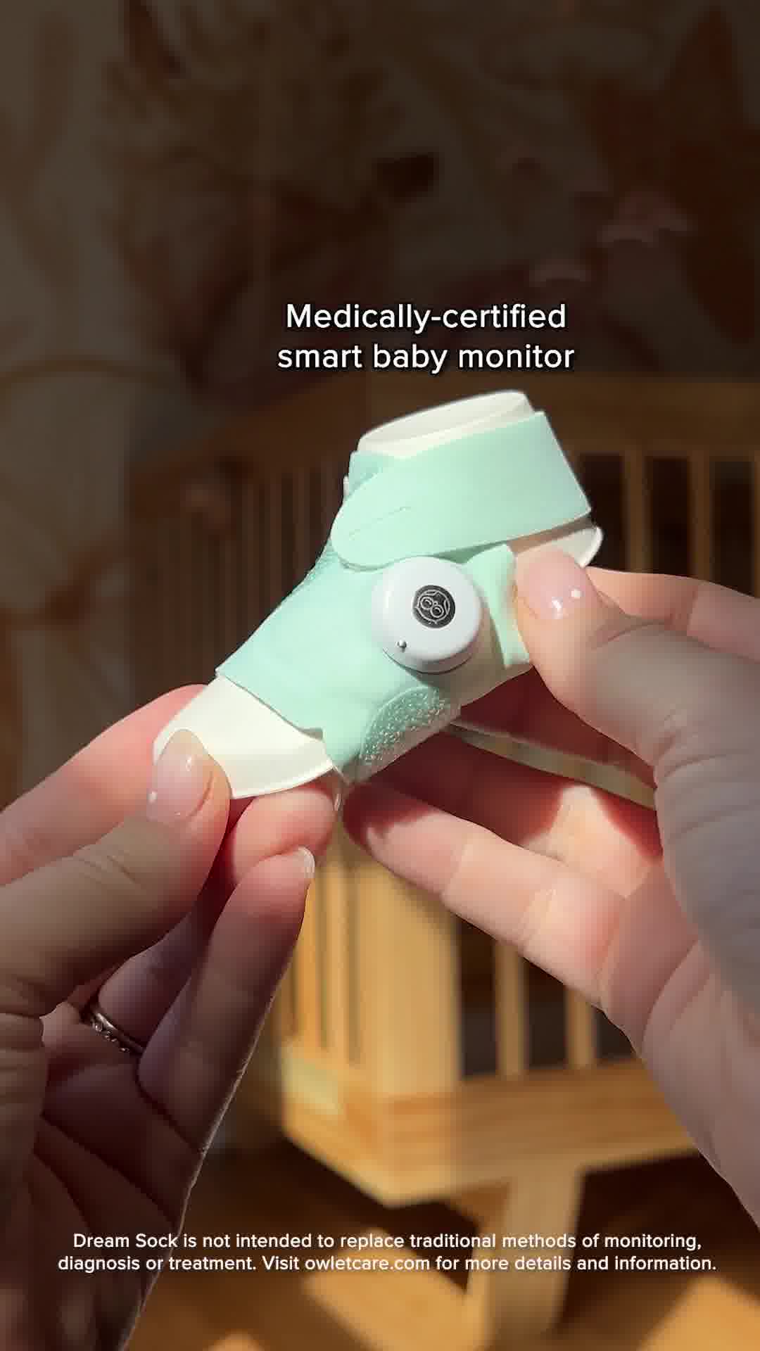 A close-up shot shows a person's hands holding a light green baby sock monitor. The monitor is wrapped around a baby's foot, with a small white circular device attached to the top. Text overlaying the image reads "Medically-certified smart baby monitor" and "Dream Sock is not intended to replace traditional methods of monitoring, diagnosis or treatment. Visit owletcare.com for more details and information."