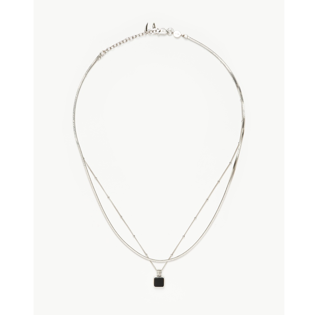 A product image of a silver necklace with a small black square pendant. The necklace is displayed against a plain white background. The text overlay advertises a free gift with purchase, specifically a Sunday Riley eye cream worth £32 when customers spend £100 or more.
