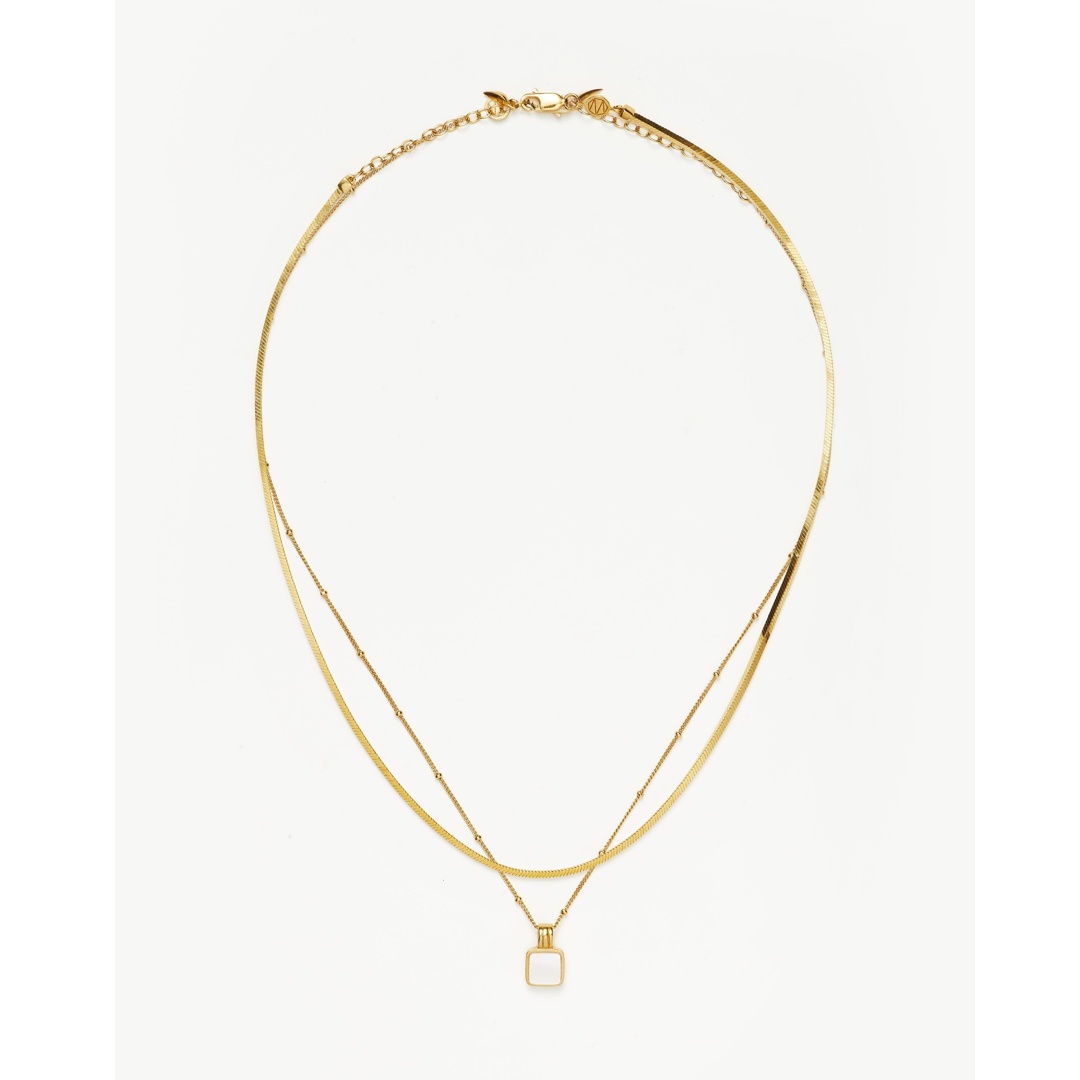A product shot of a gold necklace with a square white pendant against a white background. The necklace is layered, with a thinner chain featuring small beads and a thicker chain with a herringbone pattern. Text overlays highlight a 10% discount code for first-time orders, thousands of five-star reviews, design origin in London, and celebrity endorsement.