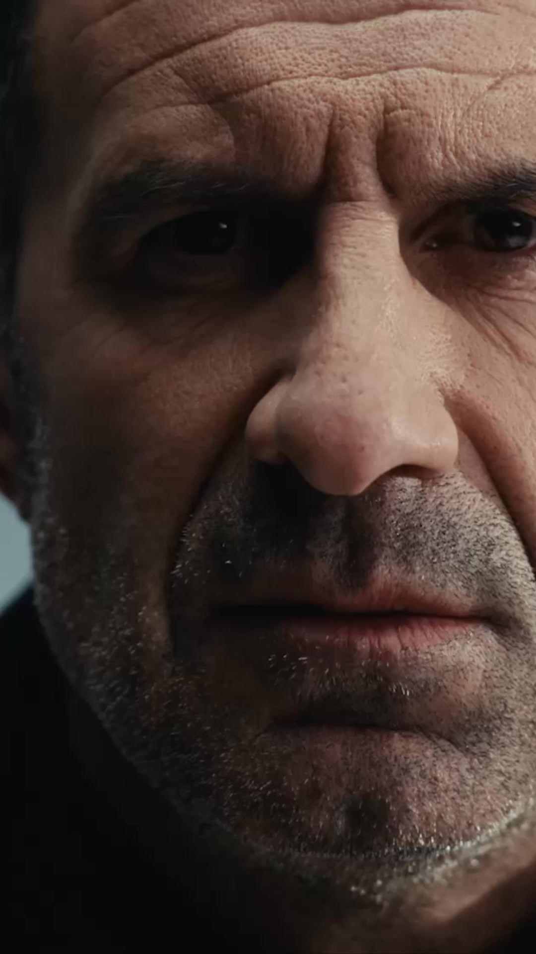A close-up, dramatic shot of an older man's face, focusing on his eyes, nose, and mouth. The lighting is dim, creating shadows that emphasize the lines and texture of his skin. The text "You're not alone." is overlaid in a stark white font across the image. The overall impression is one of intensity and perhaps shared struggle or understanding.