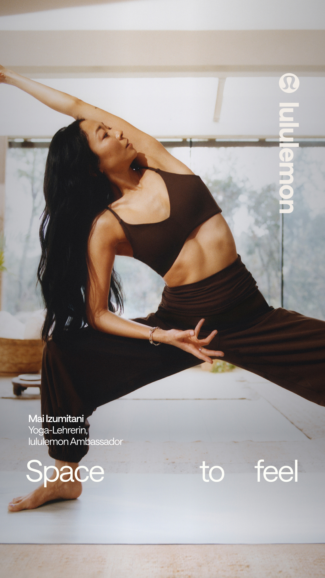 A woman of Asian descent, identified as Mai Izumitani, a Yoga-Lehrerin and lululemon Ambassador, is captured in a dynamic yoga pose, specifically the Extended Side Angle pose. She is wearing a dark brown yoga set and is positioned on a yoga mat. The background features a blurred view of trees and natural light streaming in, creating a serene atmosphere. Overlaid on the image are the words "Space to feel", suggesting a theme of mindfulness and personal space. The lululemon logo is subtly placed on the right side of the image.