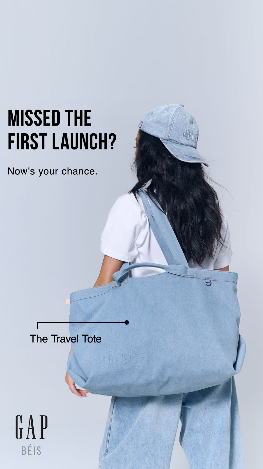 A woman wearing a denim cap and a white t-shirt is shown from behind, holding a large light blue denim tote bag. The tote bag has "GAP" embossed on it. Text on the left side of the image reads "MISSED THE FIRST LAUNCH?" followed by "Now's your chance." A line points to the tote bag with the text "The Travel Tote" below it. The GAP BÉIS logo is in the bottom left corner.