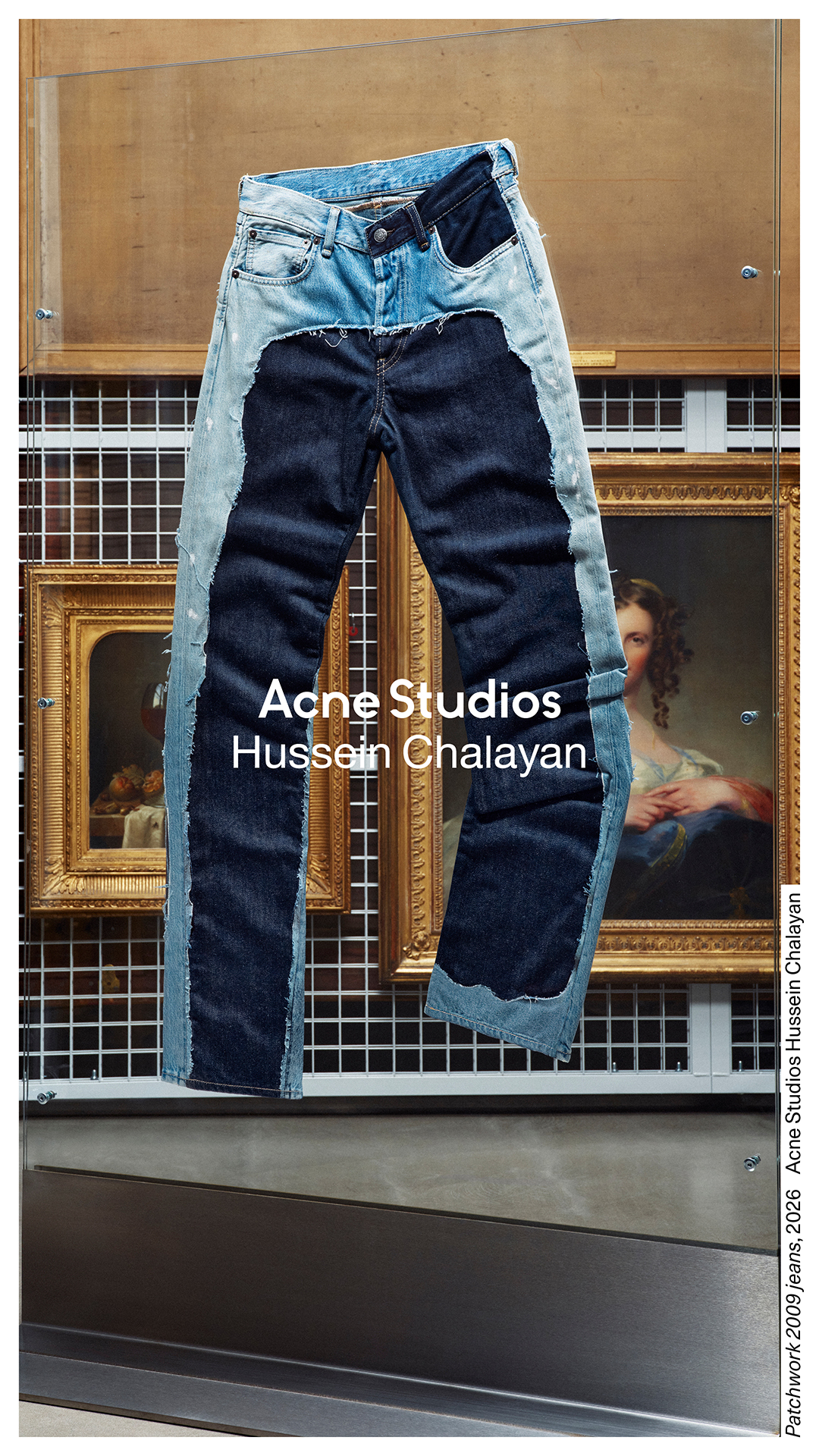 A pair of deconstructed jeans is displayed against a backdrop of framed artwork. The jeans are a patchwork of light and dark denim, with raw edges and visible stitching. Text overlayed on the image reads "Acne Studios Hussein Chalayan." The creative highlights a collaboration reinterpreting Chalayan’s design hallmarks in Acne Studios foundational materials, drawing on seminal collections from the designer’s oeuvre in the early 2000s.