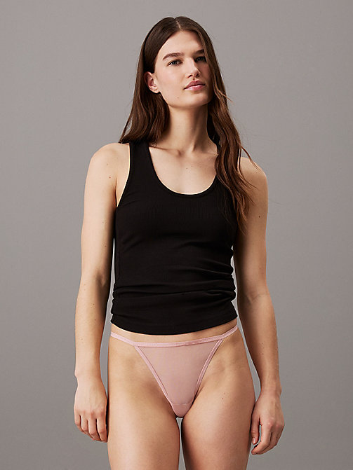 A model stands against a plain grey background, wearing a black ribbed tank top and a light pink thong. The model is looking directly at the camera with a neutral expression. The text "Shop your Calvin Klein favourites." is overlaid in white sans-serif font at the bottom of the image.