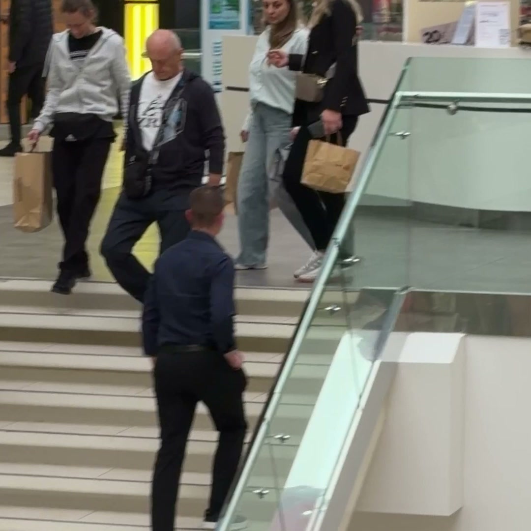 A group of people are walking up a set of stairs in what appears to be a shopping mall. The person in the foreground is wearing a dark blue shirt and black pants, walking away from the camera. Other shoppers are visible in the background, some carrying shopping bags. Overlayed text reads: "The countdown to madness begins. ⏳ Subscribe to Black Friday Early Access and unlock extra discounts!"