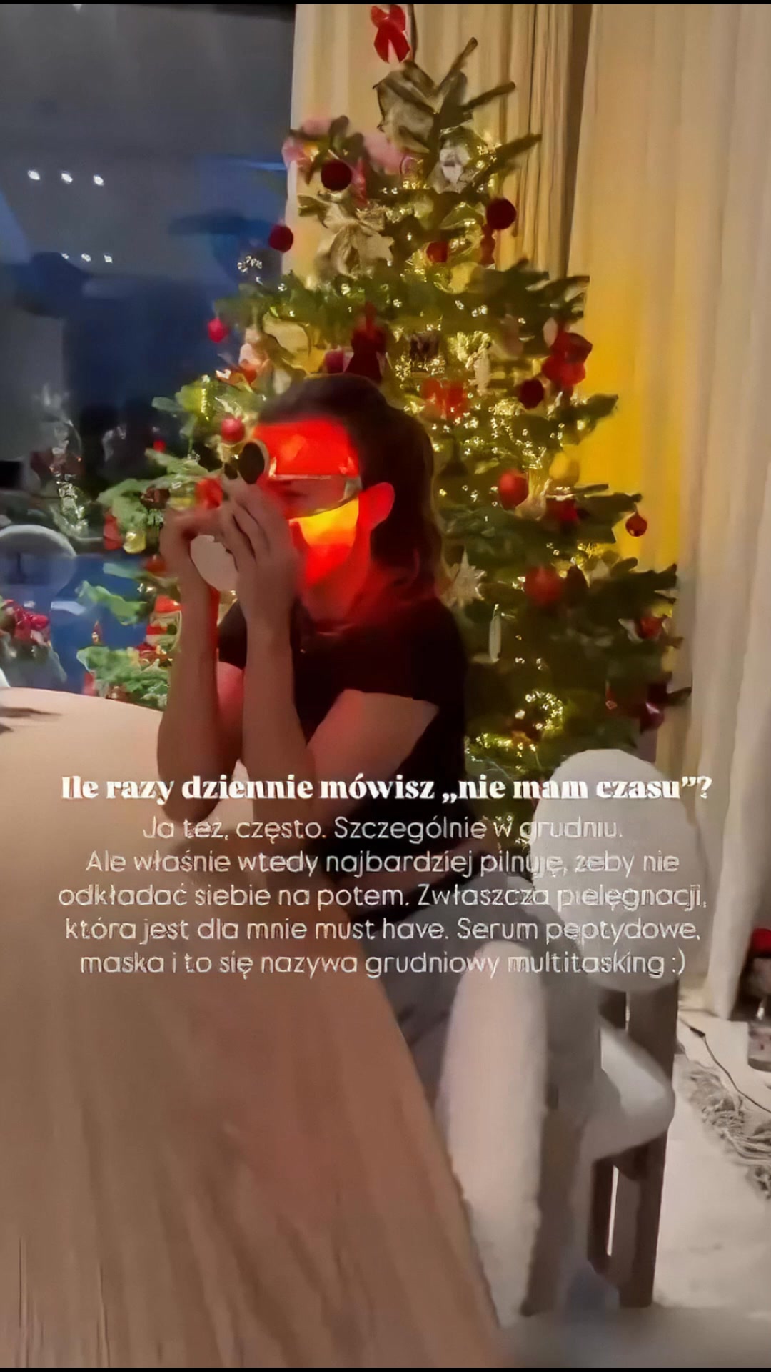 A woman is holding a red light therapy mask to her face in front of a decorated Christmas tree. The text on the screen asks, "How many times a day do you say 'I don't have time'?" Below that, it says, "Me too, often. Especially in December. But that's exactly when it's most important not to postpone yourself for later. Especially skincare, which is a must-have for me. Peptide serum, mask and this is called December multitasking :)"