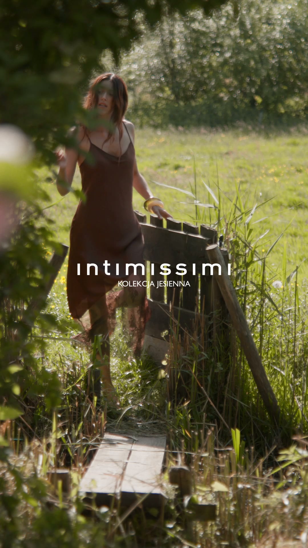 A woman in a brown slip dress walks across a wooden bridge in a grassy, outdoor setting. The Intimissimi logo and the text "KOLEKCJA JESIENNA" (Autumn Collection) are overlaid on the image. The hook, "Nowy sezon, nowe inspiracje." (New season, new inspirations.), suggests a fresh start and new ideas related to the season.
