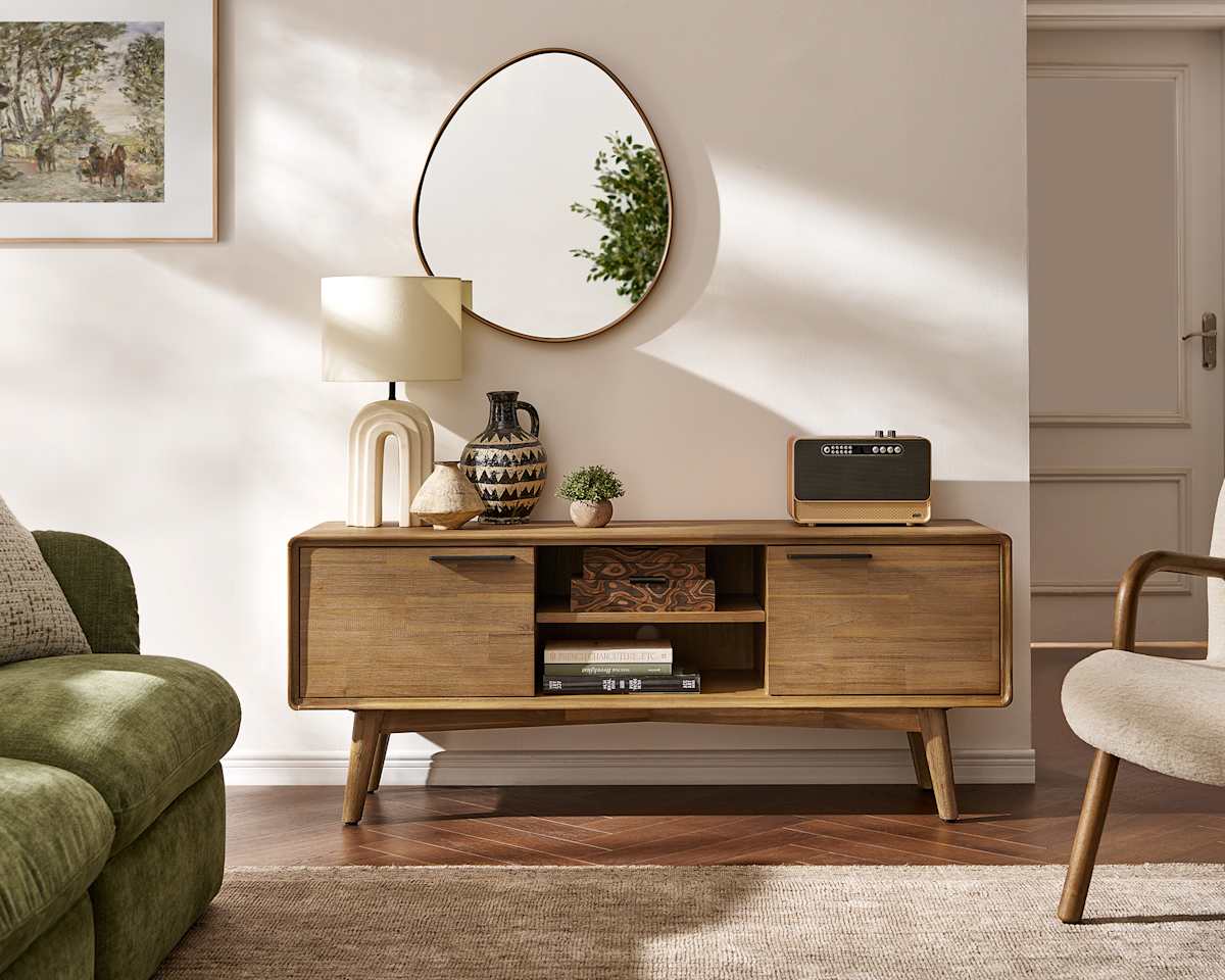 A beautifully styled living room scene features a modern wooden media console. On the console are decorative items like a lamp, a vase, and a small plant, along with a vintage-style speaker. The overall aesthetic is warm and inviting, showcasing the furniture as part of a comfortable home environment. The text overlay highlights the durability and multifunctionality of the new arrivals.