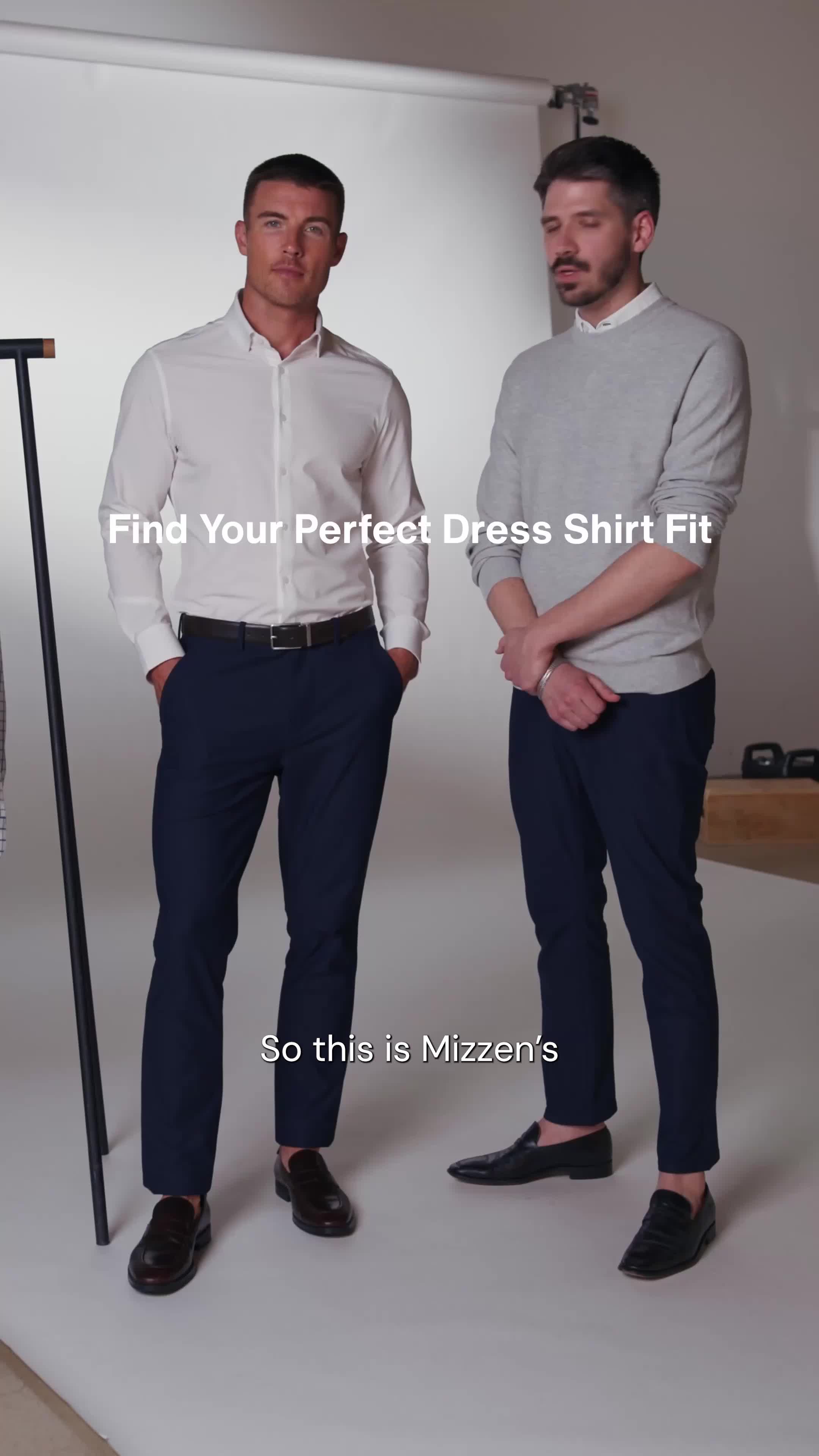 Two men are standing in front of a plain background. The man on the left is wearing a white dress shirt and navy pants. The man on the right is wearing a grey sweater over a white collared shirt and navy pants. White text overlaid on the image reads "Find Your Perfect Dress Shirt Fit". Below the men, more white text reads "So this is Mizzen's". The creative appears to be demonstrating different fits for dress shirts.
