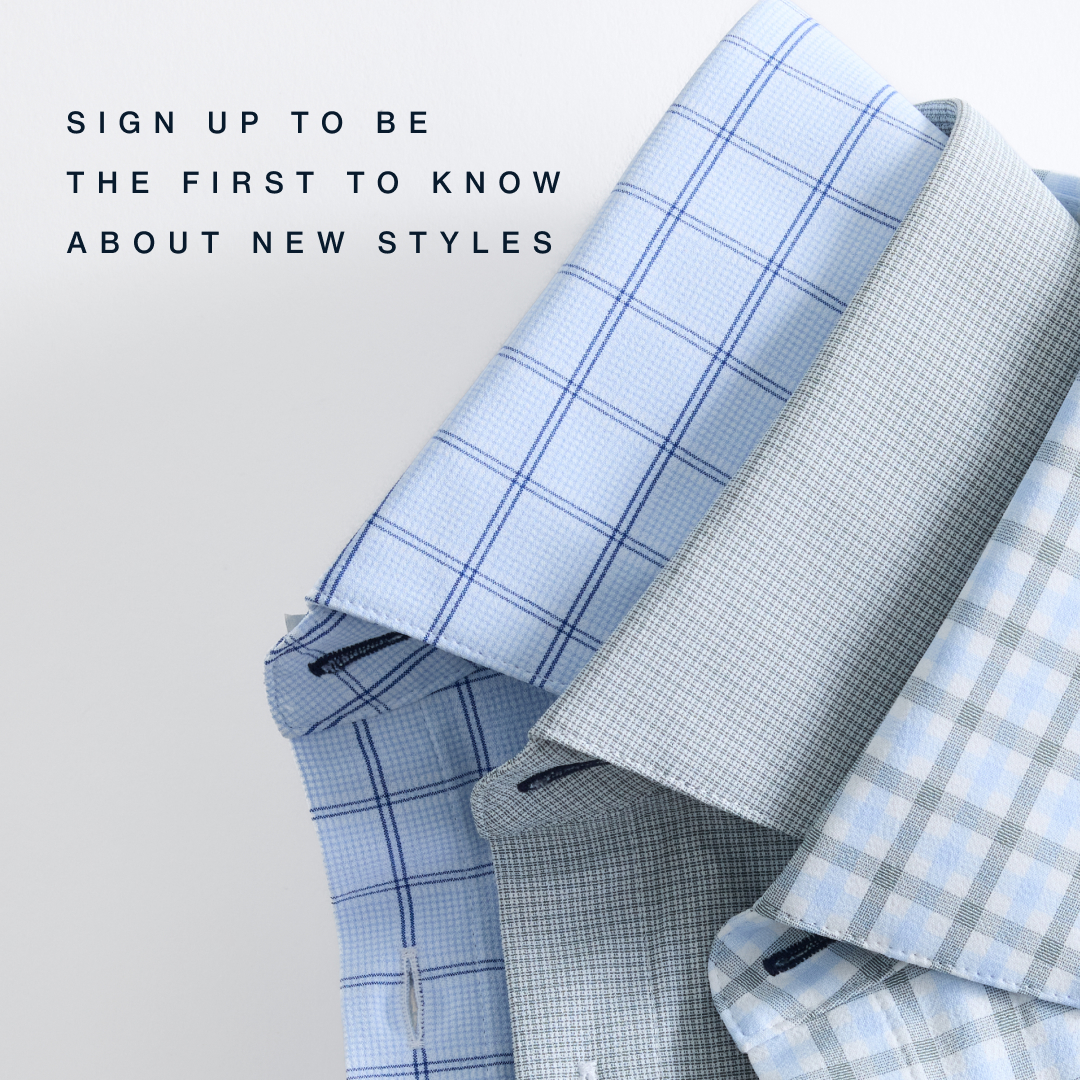 The image displays a close-up view of several folded men's dress shirts, showcasing different subtle patterns in shades of blue and grey. The shirts are neatly stacked and angled, with their collars and folded sleeves visible against a plain, light-colored background. Overlayed on the left side of the image, in a clean, sans-serif font, is the text "SIGN UP TO BE THE FIRST TO KNOW ABOUT NEW STYLES." The creative focuses on the visual appeal of the shirts and the call to action for new style notifications.