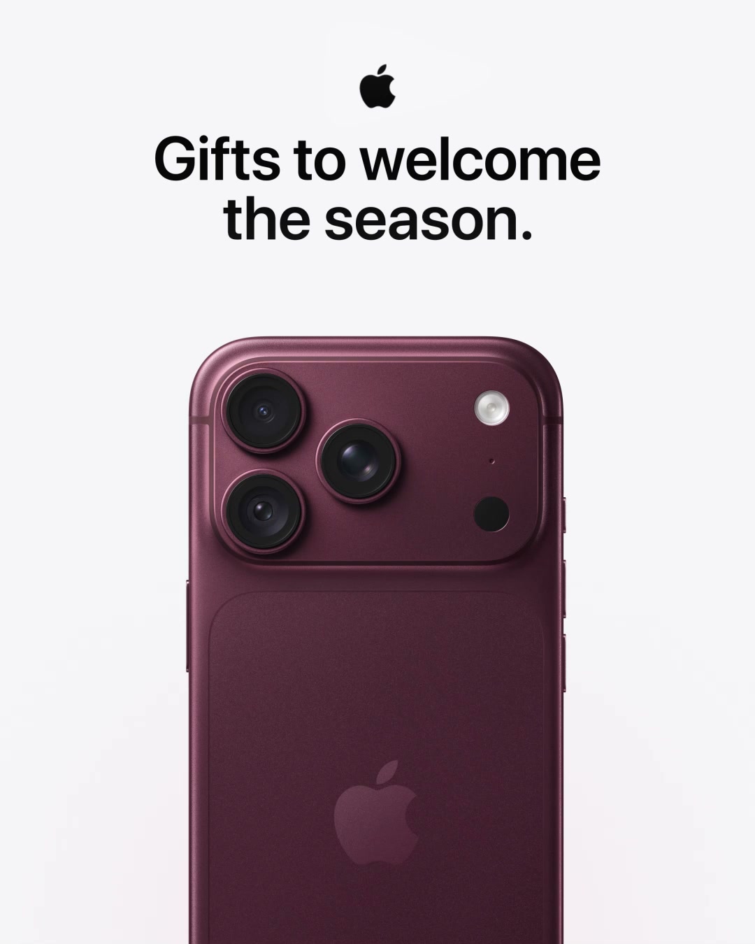 A close-up shot of the back of a dark red iPhone is shown against a white background. The Apple logo is visible in the center of the phone. Above the phone, the text "Gifts to welcome the season." is displayed in black, bold font, with the Apple logo centered above the text. The image focuses on the camera array of the phone, highlighting its design and features.