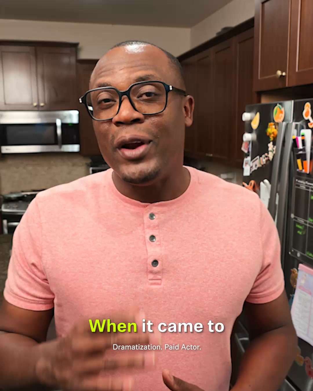 A man wearing glasses and a pink t-shirt is speaking directly to the camera in what appears to be a kitchen. Text overlays on the screen read "When it came to" in bright yellow, followed by smaller text below that says "Dramatization. Paid Actor." The man is gesturing with his hands as he speaks. The background shows kitchen cabinets and a refrigerator.