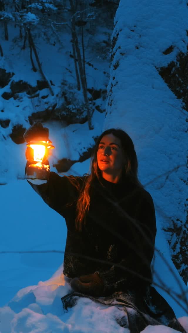 A woman sits in a snowy, wooded area at dusk, holding a lit lantern. The lantern casts a warm glow on her face and the surrounding snow. The background is dark with trees and snow-covered rocks. Text overlays the image, announcing a spring sale with up to 60% off and a discount code.