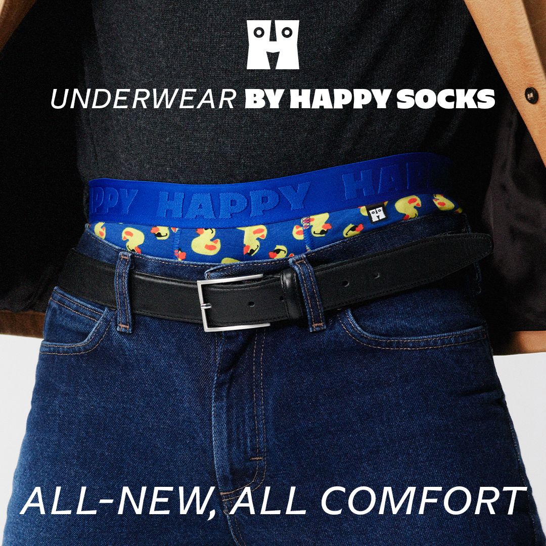 A close-up shot focuses on the waistband of men's underwear featuring a playful duck pattern, layered over a blue waistband with the "Happy" logo. The underwear is worn with dark denim jeans and a black belt. White text overlays the bottom of the image, reading "ALL-NEW, ALL COMFORT". The top of the image shows the "Happy Socks" logo and text that reads "UNDERWEAR BY HAPPY SOCKS".