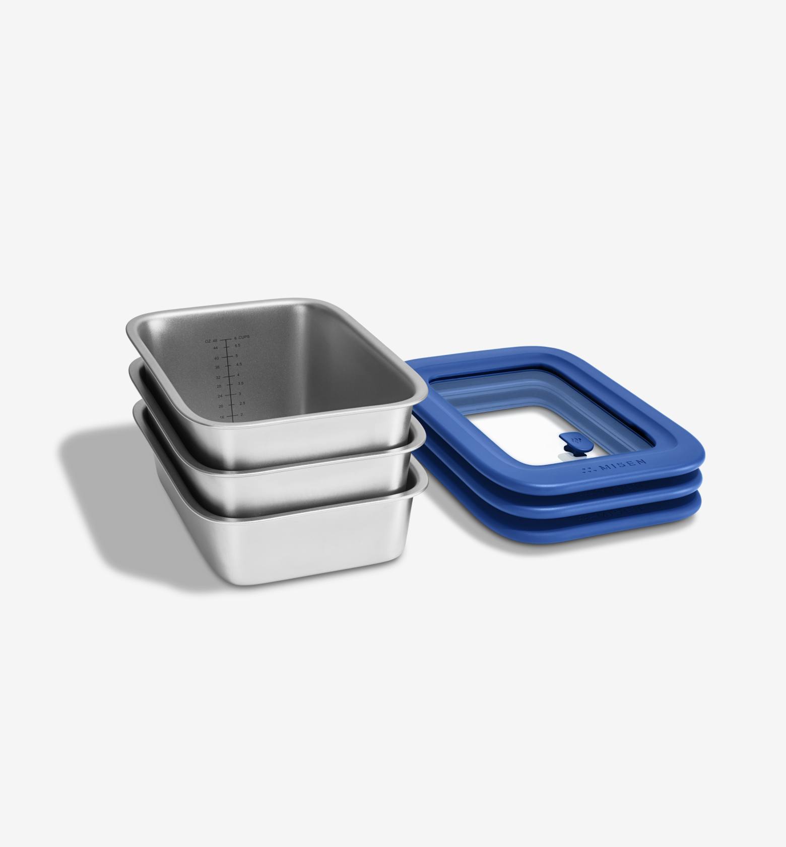 A studio shot shows three identical stainless steel rectangular food storage containers stacked on top of each other. To the right of the containers is a blue silicone lid, folded in half. The containers have measurement markings on the inside. The text "Three stackable sizes, one universal lid." is overlaid on the image. The copy "Oven, freezer, microwave: Misenware does it all." is also present.