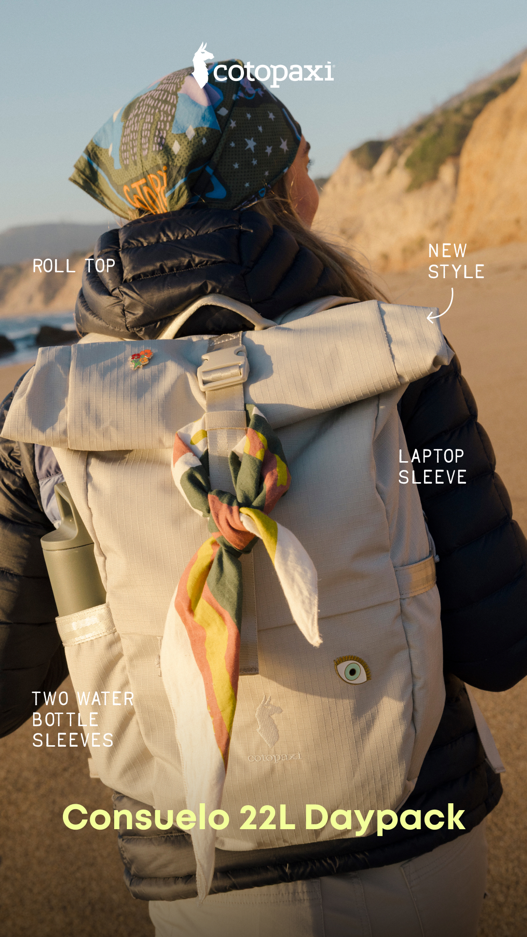 A person is shown from behind, wearing a black puffer jacket and a light-colored backpack on a beach. Text overlays highlight features of the backpack: "ROLL TOP", "NEW STYLE", "LAPTOP SLEEVE", and "TWO WATER BOTTLE SLEEVES". The backpack has a colorful scarf tied to it and a small pin with flowers. The brand logo "cotopaxi" is visible at the top, and the product name "Consuelo 22L Daypack" is displayed prominently at the bottom.