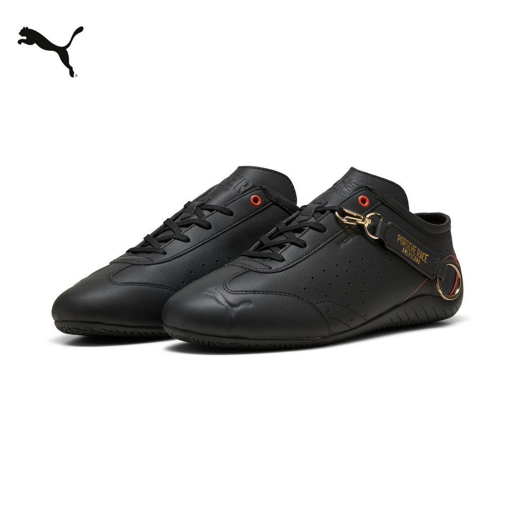 A pair of black Puma sneakers with orange accents and gold hardware is shown against a white background. The Puma logo is visible on the left shoe. Text overlays the image, stating "Un icono de la sencillez que se adapta a tu estilo de diario. Compra ahora." The shoes have a sleek, low-profile design, with perforations on the side and the "PORSCHE RACE AMERICANA" branding on the heel strap.