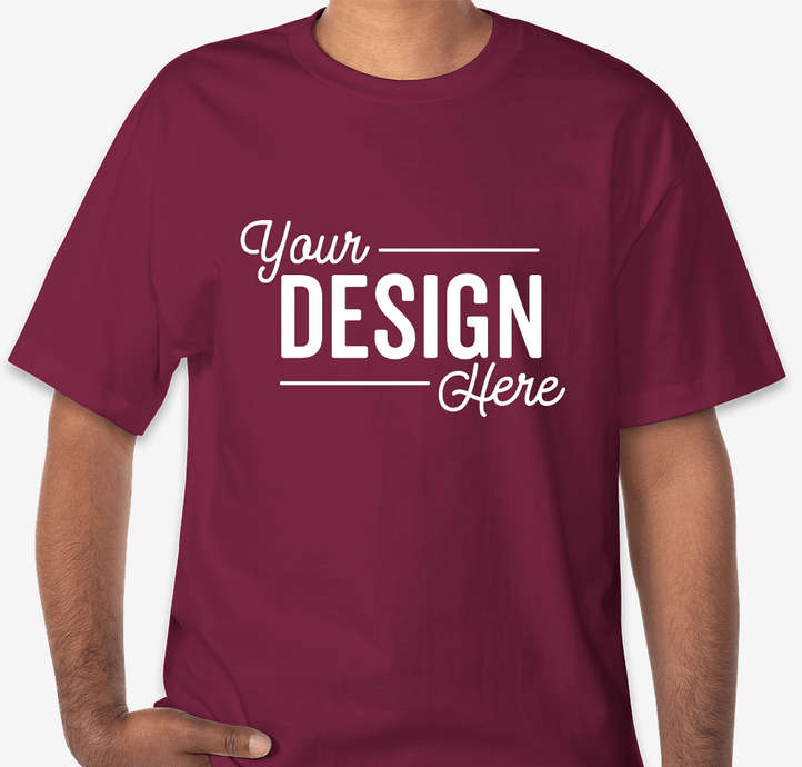 A maroon t-shirt is shown from the chest up, with a white text overlay that reads "Your Design Here." The text is stylized with "Your" in a script font, "DESIGN" in a bold sans-serif font, and "Here" in a script font below "DESIGN." The t-shirt is on a person, with their arm bent and hand resting on their hip. The background is a plain light gray. The creative is a product mockup for custom t-shirt printing.