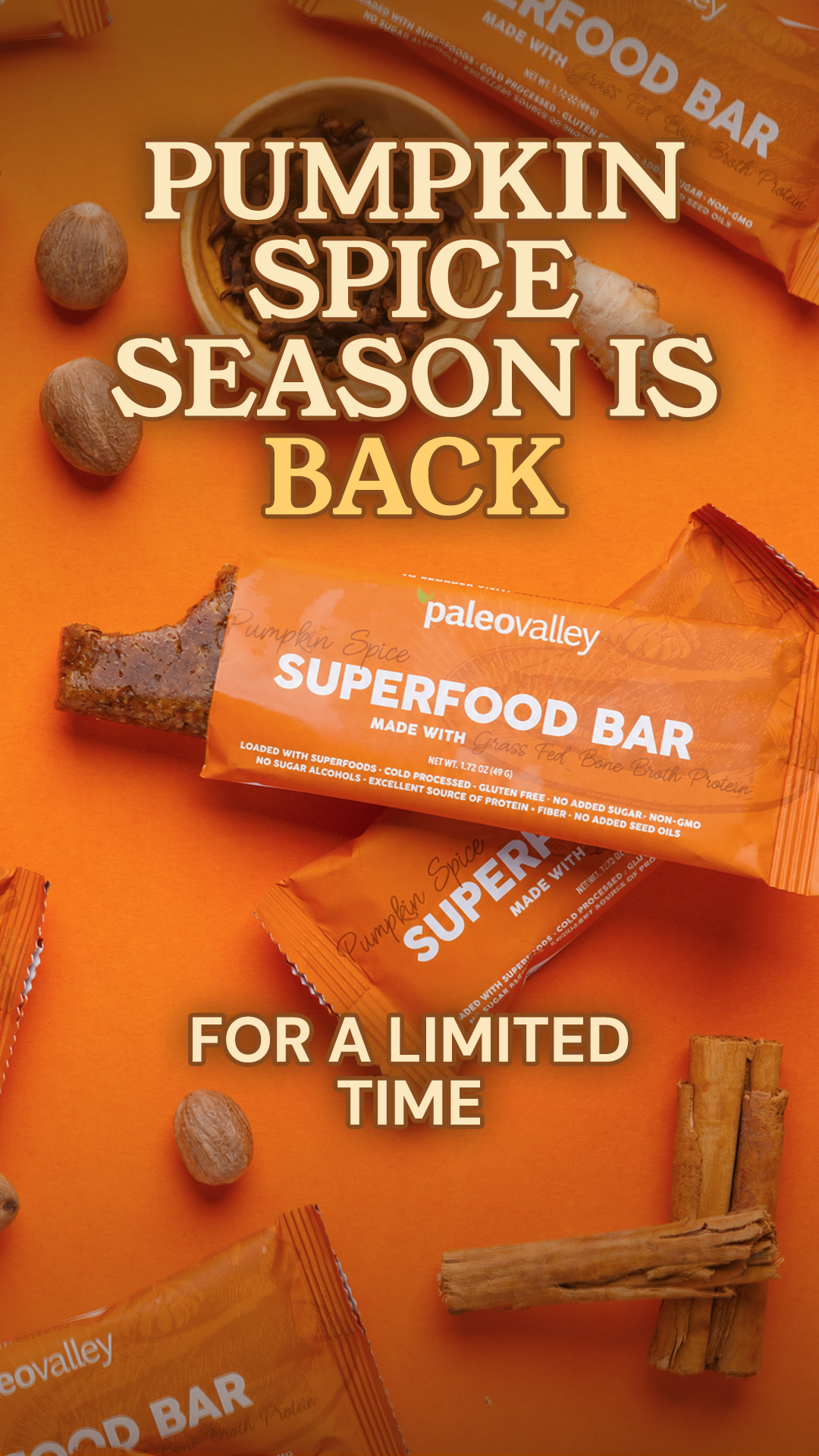 The image features Paleovalley Superfood Bars with a "Pumpkin Spice Season Is Back" headline. The bars are orange with "Paleovalley Superfood Bar" text. The background is a vibrant orange, with whole nutmeg and cinnamon sticks scattered around. A portion of one bar is bitten off, revealing its texture. Below the main headline, text reads "FOR A LIMITED TIME". The overall aesthetic is autumnal and emphasizes the seasonal availability of the product.