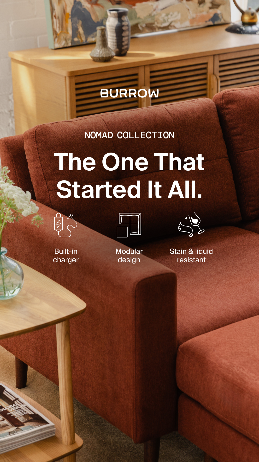 A close-up shot of a rust-colored sofa with wooden legs and a small wooden side table. The sofa has three icons with text below them: a battery icon labeled "Built-in charger", a grid icon labeled "Modular design", and a wine glass with a splash labeled "Stain & liquid resistant". The brand name "BURROW" is displayed prominently at the top, followed by "NOMAD COLLECTION" and the headline "The One That Started It All." The overall aesthetic is clean and modern, highlighting the product's features.