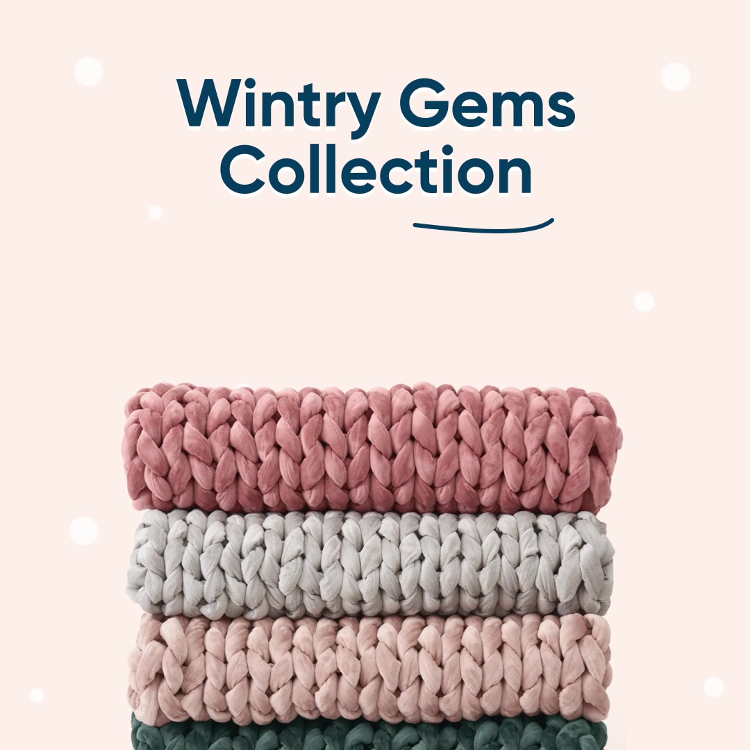 A stack of three thick, knitted blankets in muted colors (pink, grey, pink) is shown against a pale pink background with scattered white circles resembling snowflakes. The text "Wintry Gems Collection" is prominently displayed in dark blue, sans-serif font at the top of the image. Below the blankets, a subtle dark blue line underlines the collection name. The overall aesthetic is cozy and suggests a winter-themed product launch.