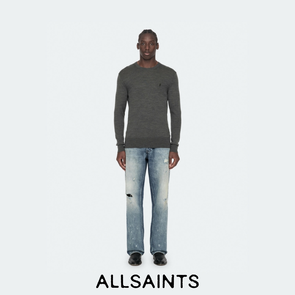 A full-body studio shot of a male model wearing a dark grey crewneck sweater and distressed light-wash jeans. The model stands against a plain white background with the AllSaints logo at the bottom center. The text overlay reads "Autumn 26: The AllSaints wardrobe is rebuilt, refitted and reworked with a new exactitude." This creative highlights the brand's new collection with a focus on precise tailoring and updated fits for the autumn season.