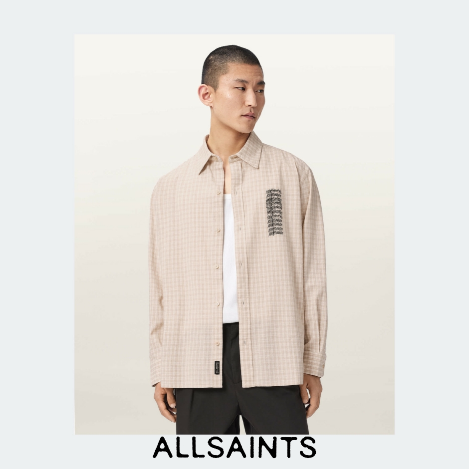 A male model stands against a neutral background, wearing a beige checkered long-sleeved shirt over a white tank top and black trousers. The shirt has a small black logo patch on the left chest. The brand name "ALLSAINTS" is displayed in large, bold, black sans-serif font at the bottom of the image. The on-screen text introduces the Fall 26 collection, emphasizing a rebuilt and reworked wardrobe with new exactitude.