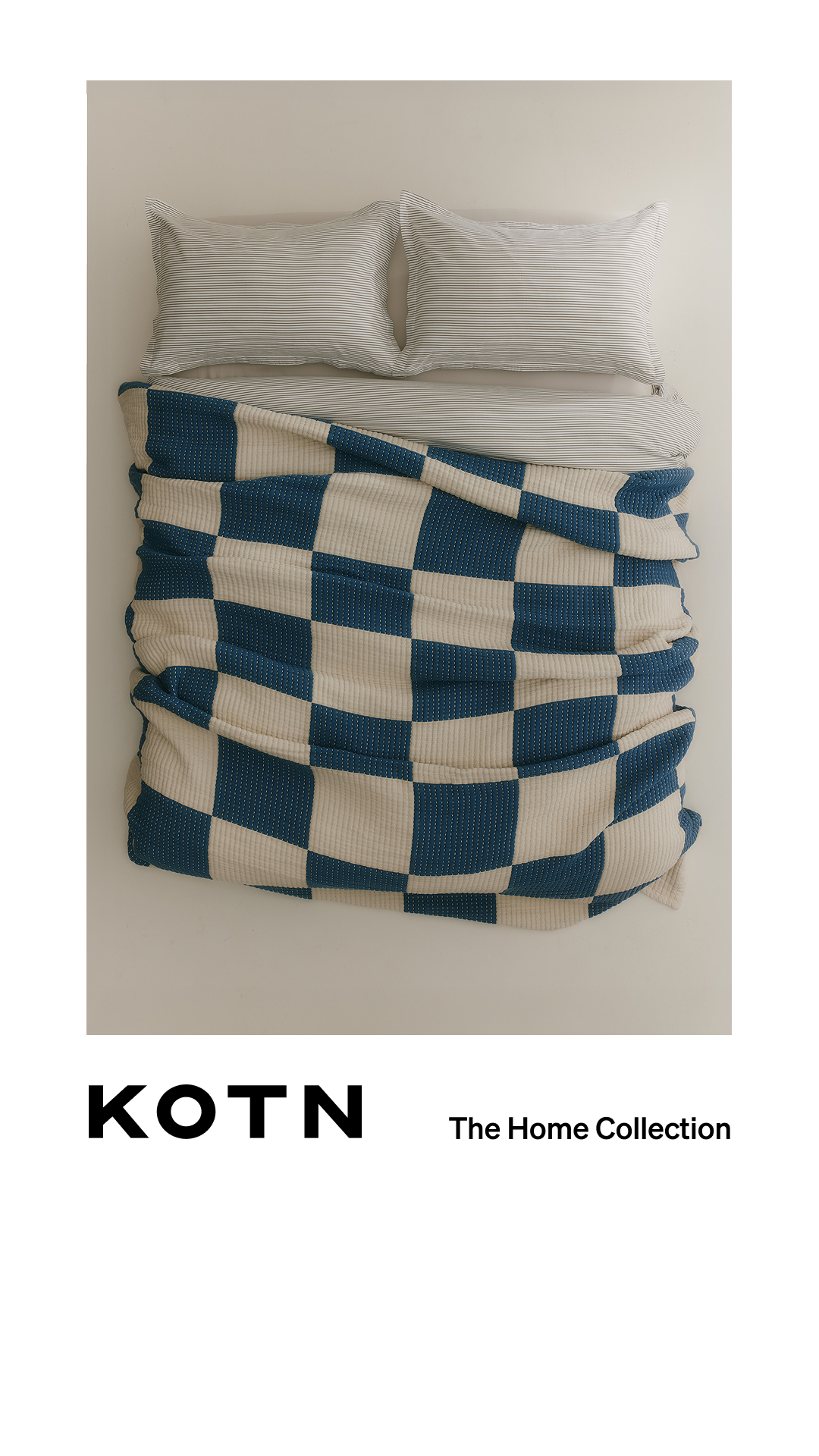 A top-down view of a neatly made bed with two pillows and a blue and cream checkered blanket draped over it. The Kotn logo is displayed prominently on the left side of the screen, with the text "The Home Collection" to its right. The hook "World-class fibres, live-in luxury." is overlaid on the image, drawing attention to the quality and comfort of the bedding.
