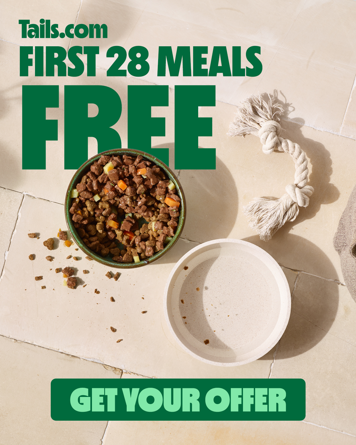 A bowl of dog food sits next to an empty dog bowl on a tiled floor. Large green text overlays the image, stating "Tails.com FIRST 28 MEALS FREE". Below the bowls, a green banner reads "GET YOUR OFFER". The overall impression is a promotional graphic for a dog food service offering a significant discount on the first month's meals.