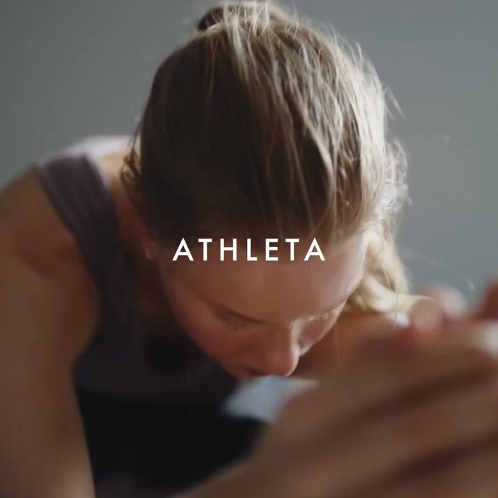 A close-up shot shows a woman with her hair in a bun, looking down with her eyes closed, appearing to be in a moment of deep concentration or relaxation. White text overlaid on the image reads "ATHLETA". The scene suggests a focus on personal well-being and athletic activity, possibly within a studio setting. The overall mood is serene and introspective, highlighting the brand's connection to fitness and mindful movement.