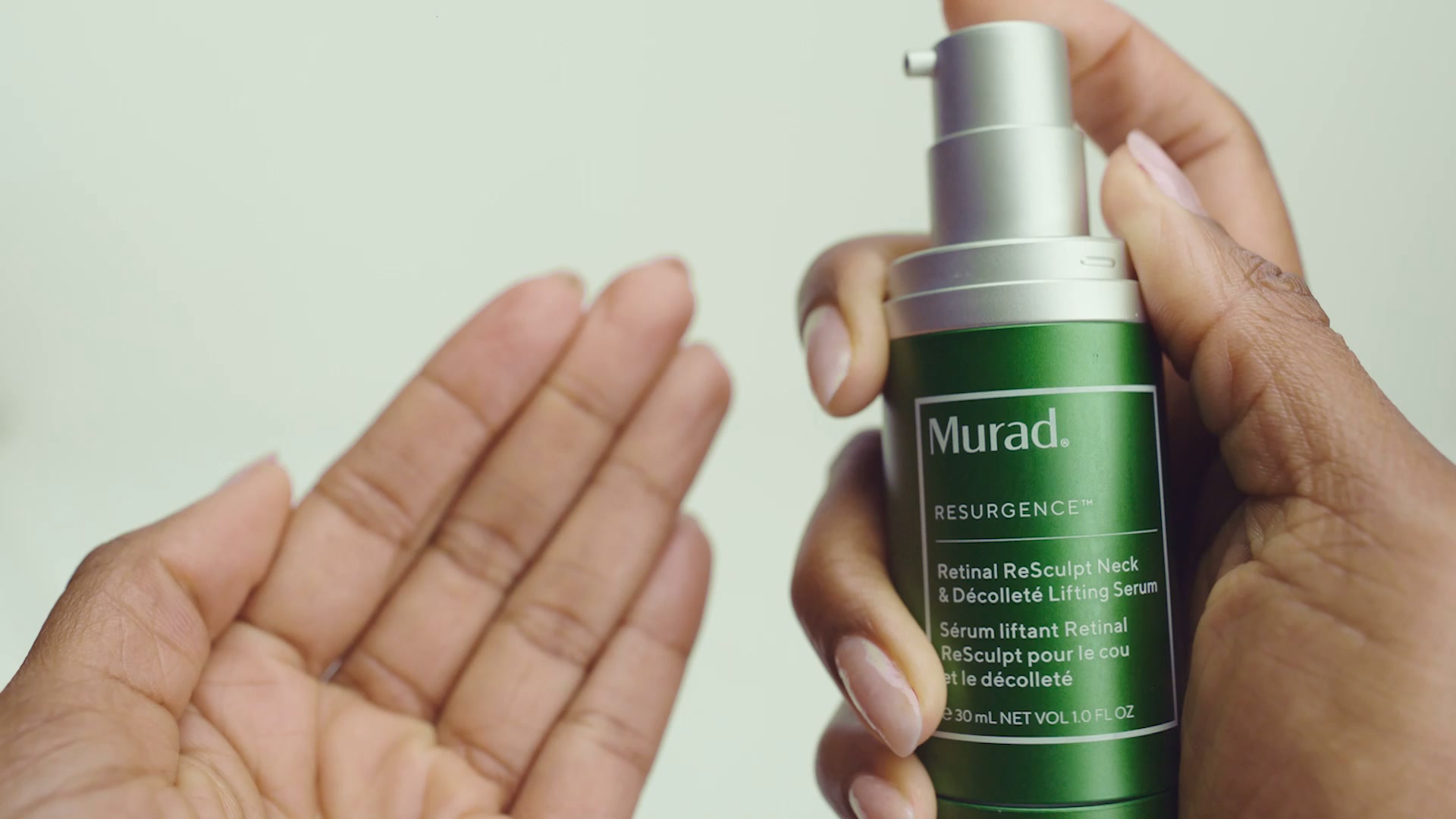A hand holds a green bottle of Murad Retinal ReSculpt Neck & Décolleté Lifting Serum. The bottle has a silver pump dispenser and a white label with black text. The text on the label is partially visible, showing the brand name "Murad" and product details. Another hand is visible on the left side of the frame, open and facing upwards. The background is a plain, light color. The on-screen text explains the serum's benefits for smoothing wrinkles and lifting sagging skin on the neck and décolleté.